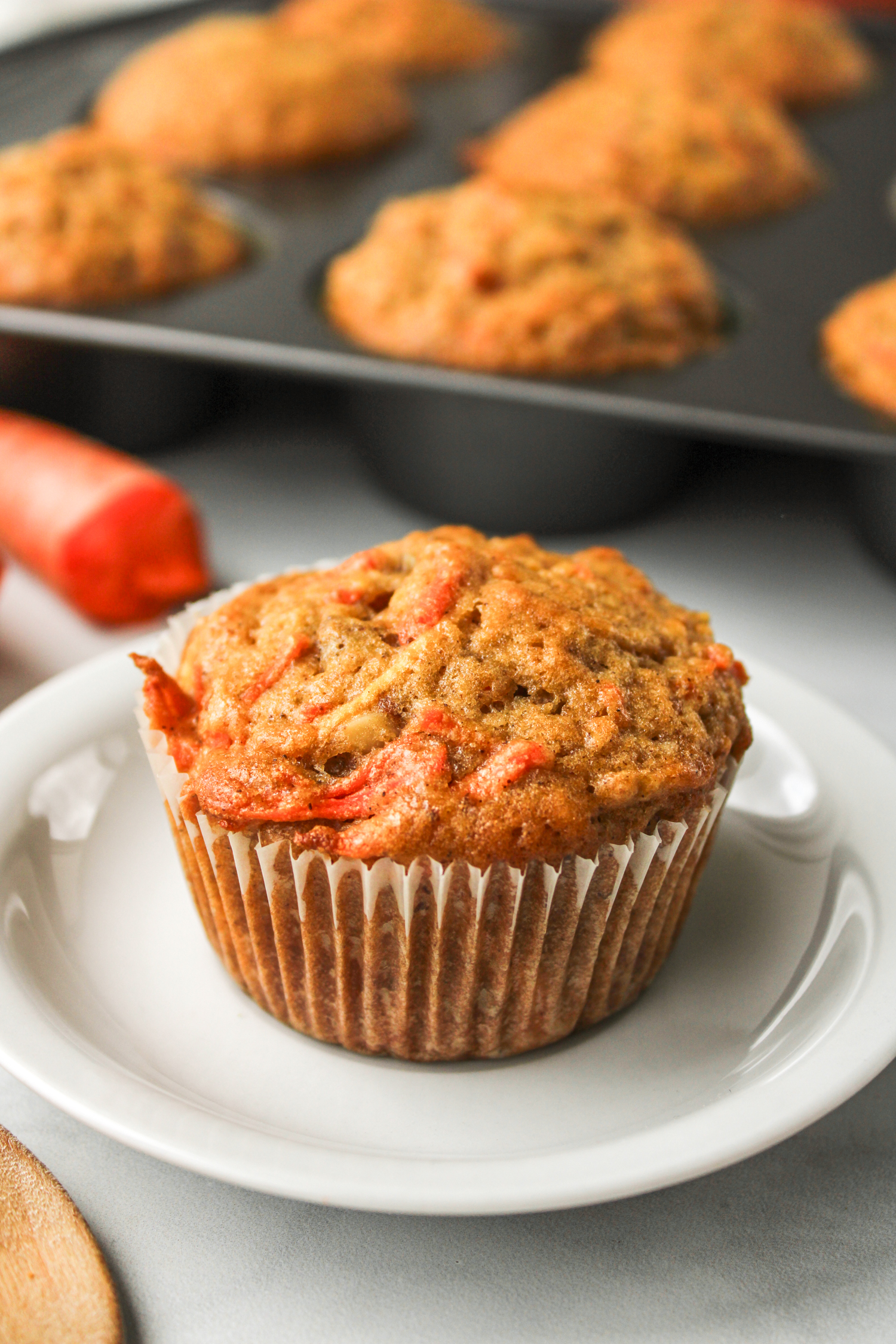 carrot apple muffin in a paper liner on a white ceramic plate