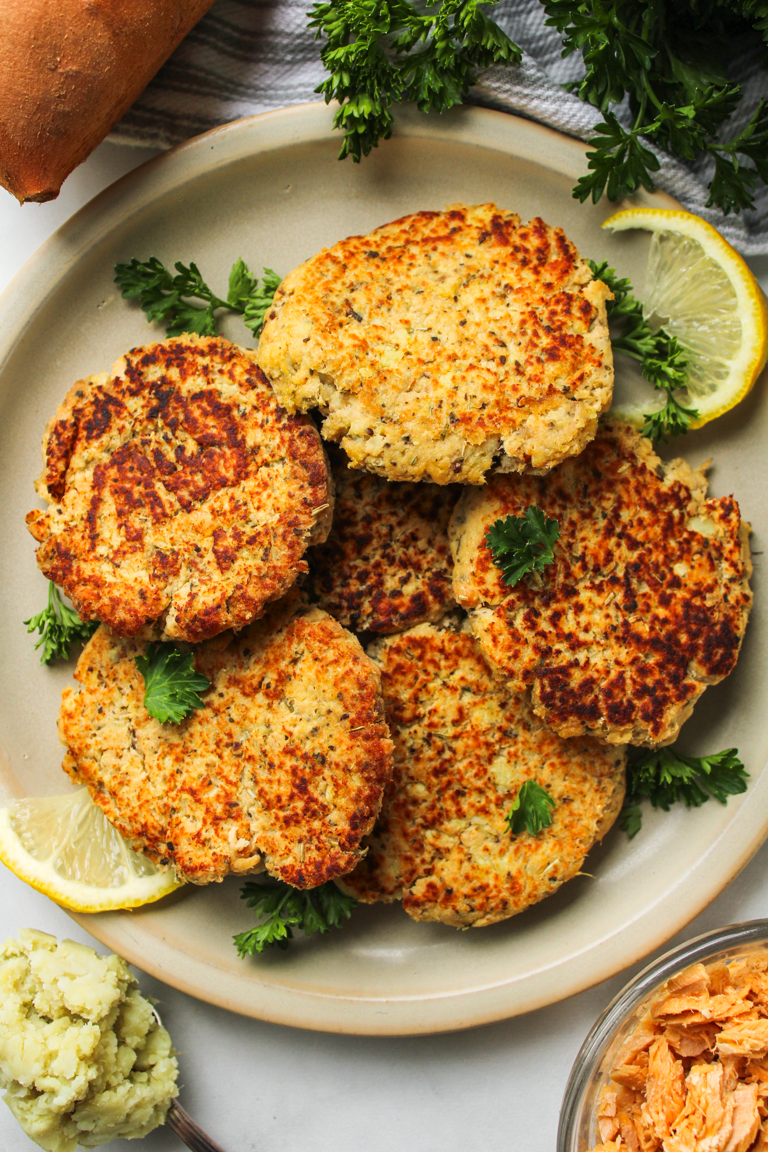 salmon sweet potato cakes on a grey ceramic plate topped with fresh parsley and ingredients around the plate