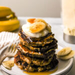 almond flour banana pancakes stacked on top of a white plate and topped with greek yogurt, banana and maple syrup