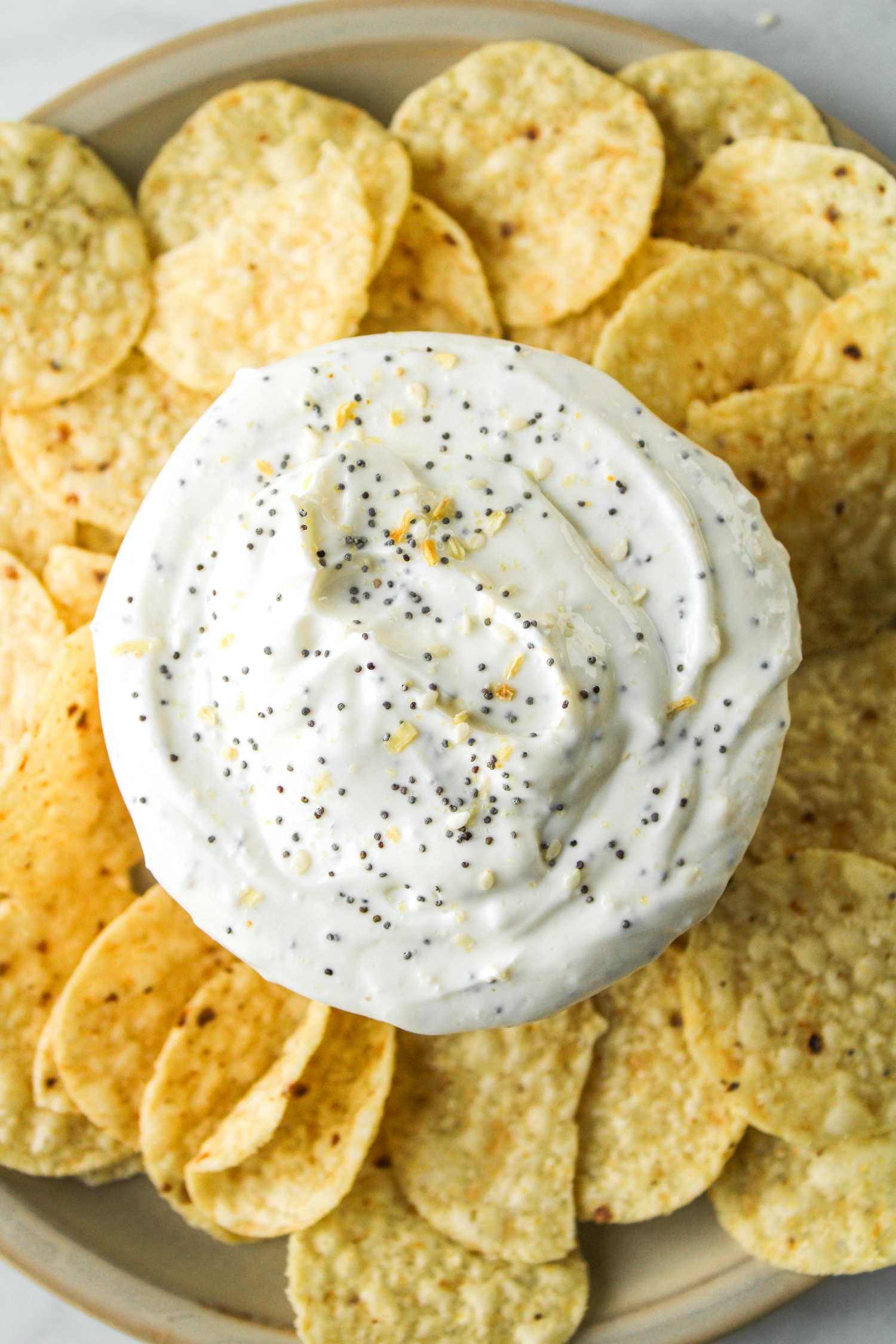 close up overhead shot of everything but the bagel dip in a white bowl surrounded by corn chips