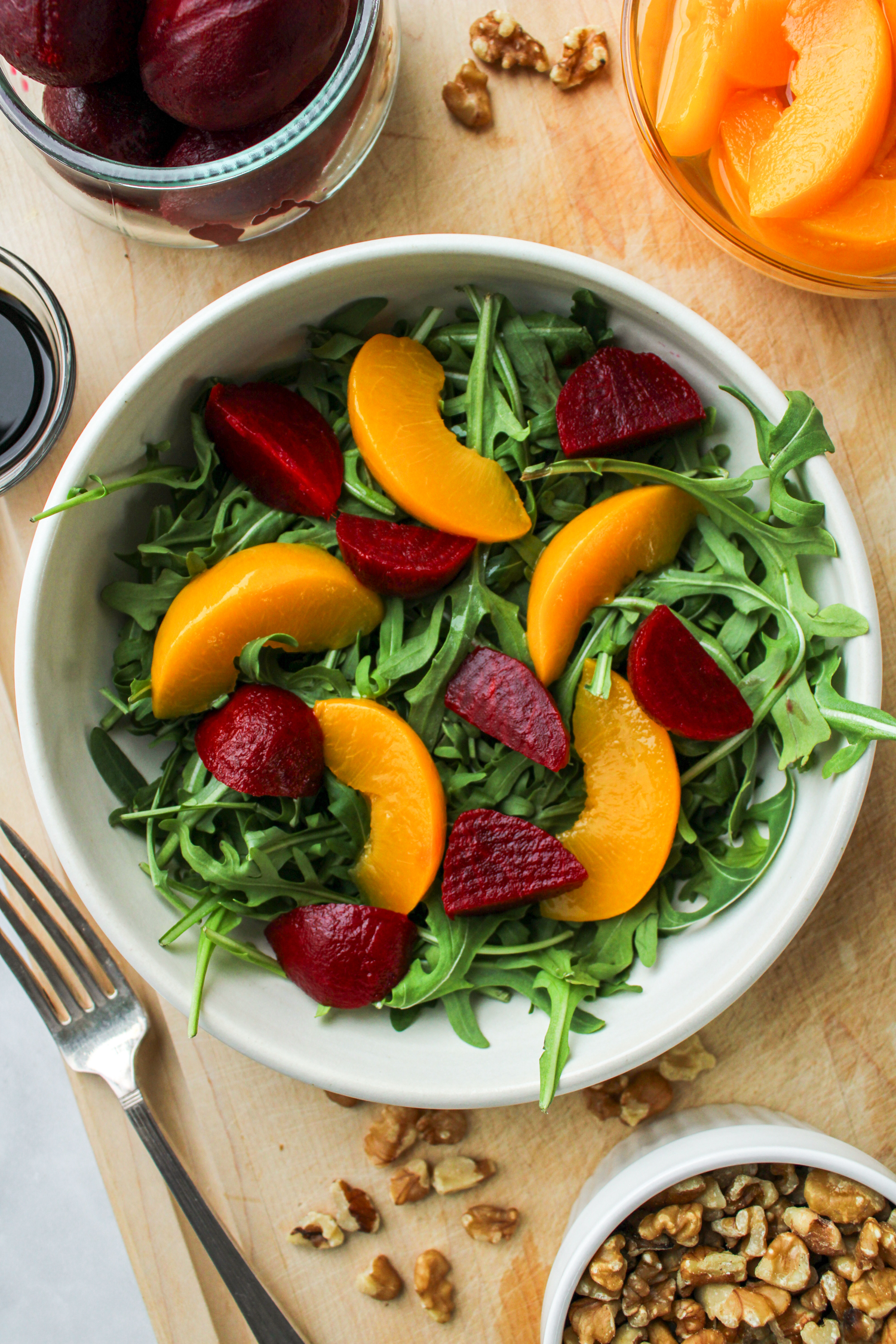 A ceramic bowl with arugula topped with sliced canned peaches and quartered beets 