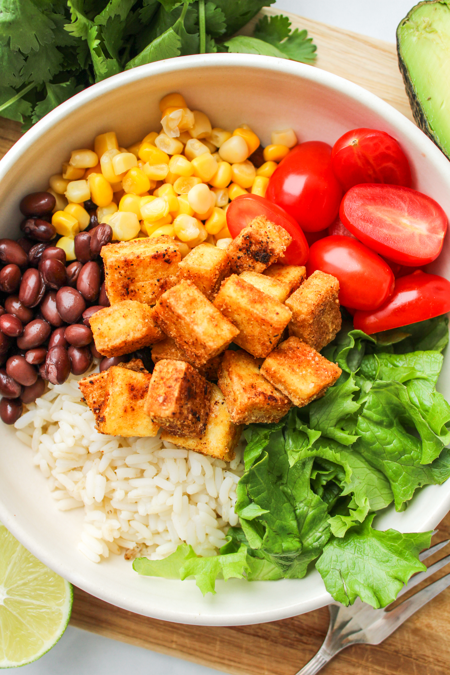 overhead shot of ingredients of the tofu burrito bowl in a white ceramic dish placed on top of a wooden cutting board