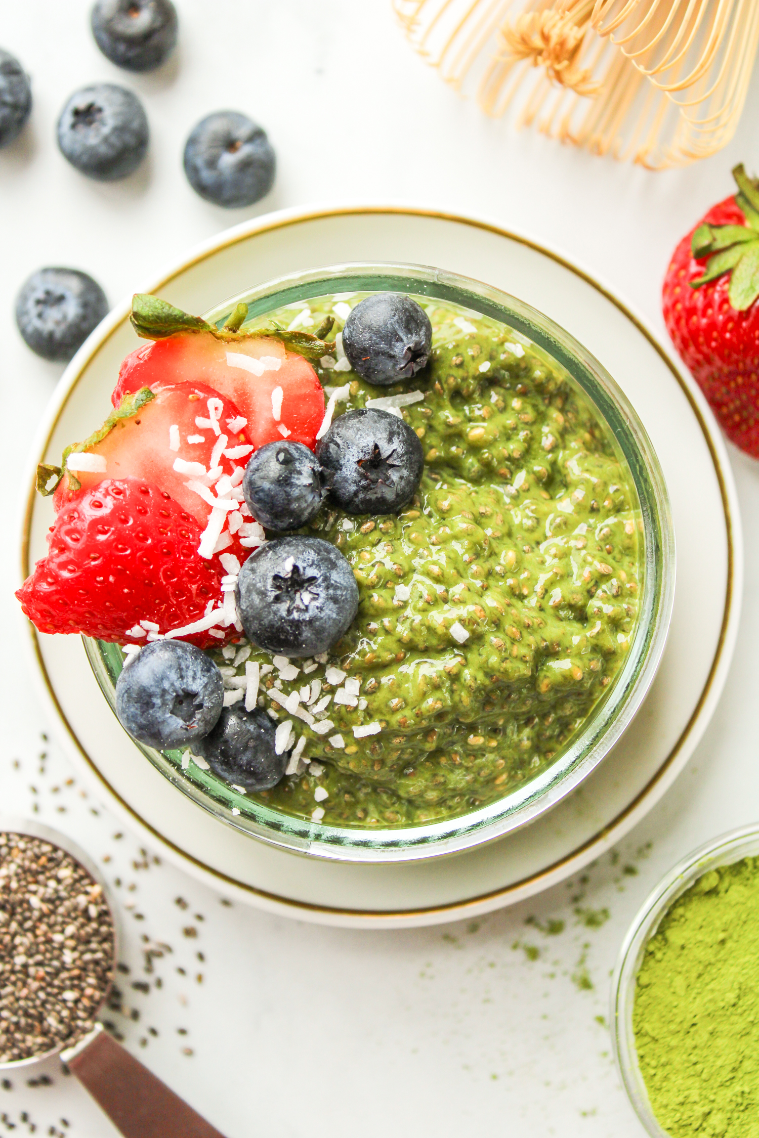 matcha chia seed pudding in a small glass bowl topped with berries and coconut flakes