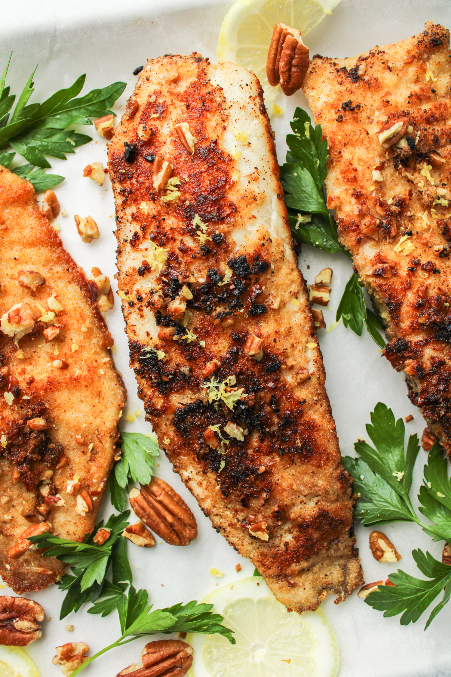 overhead shot of 3 fillets of pecan crusted tilapia topped with chopped pecans, lemon zest and parsley