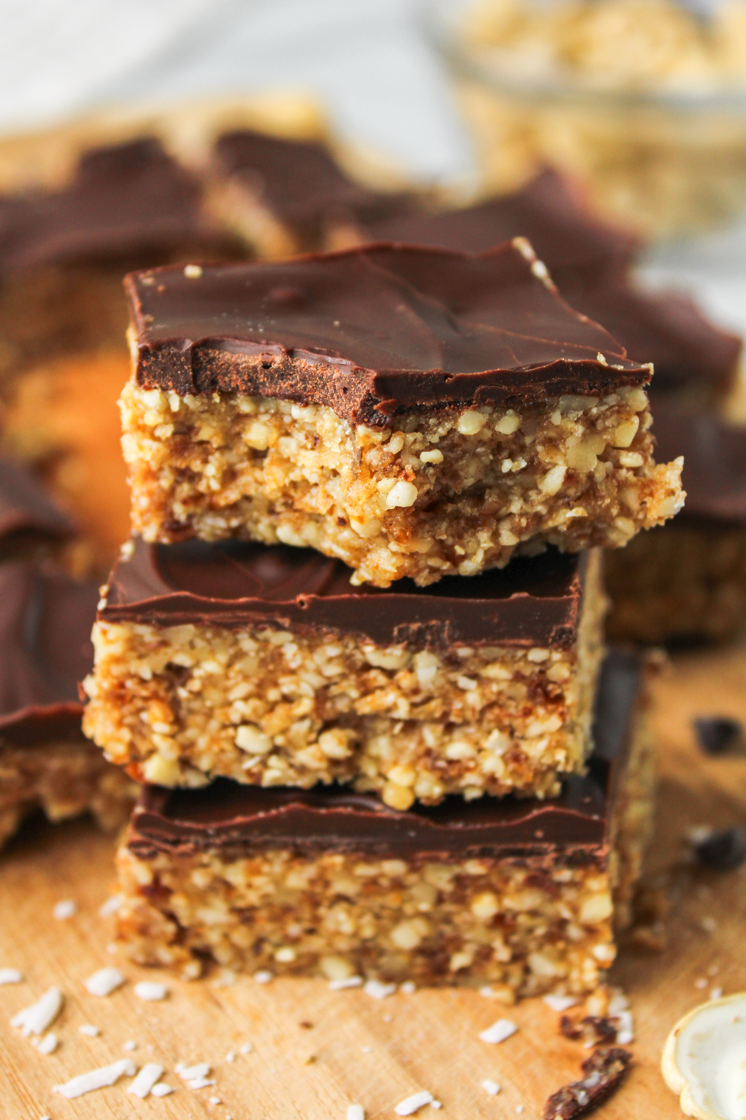 close up of 3 squares of cashew bar with chocolate coating stacked on top of each other, with a bite taken out of the top one