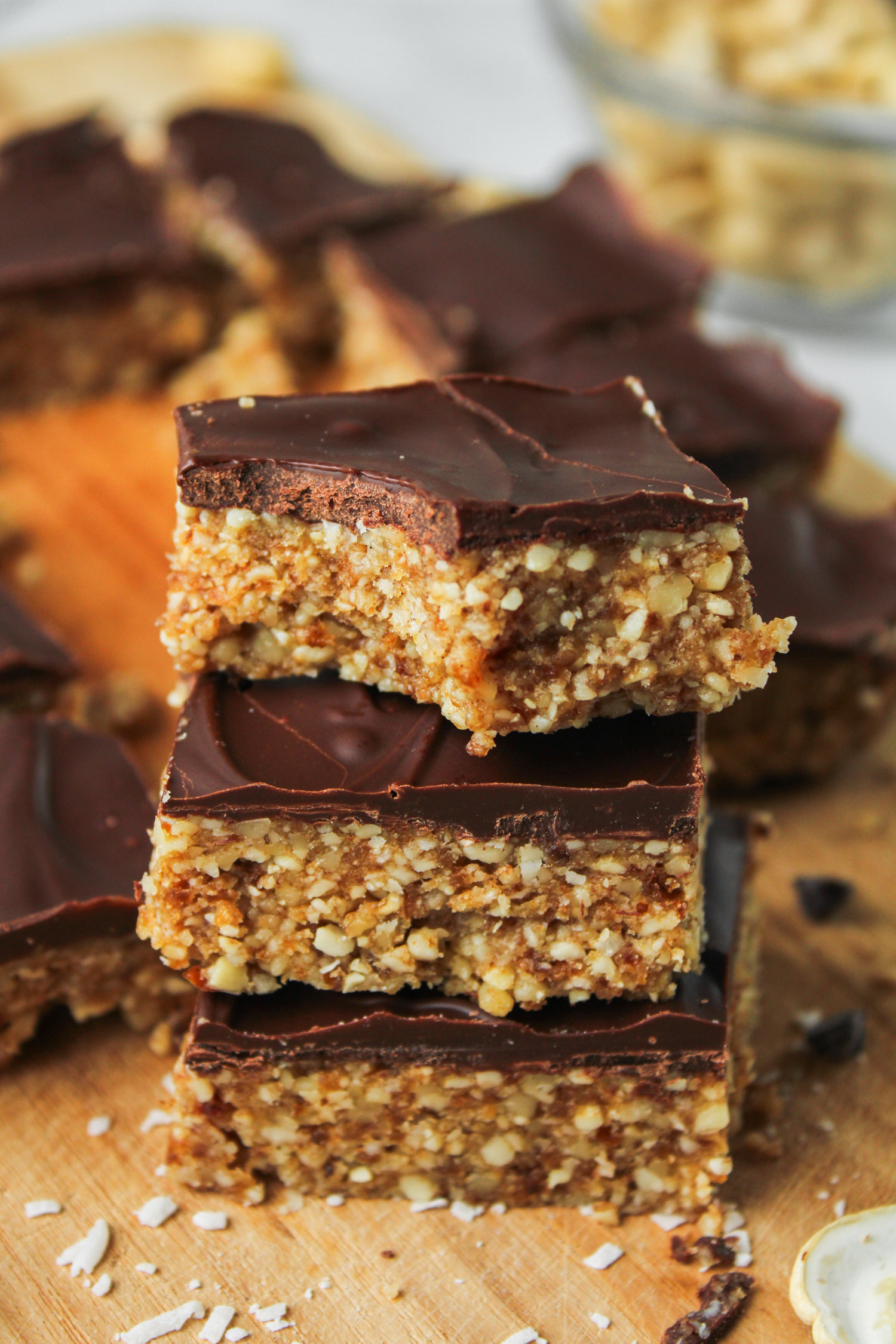 3 squares of cashew bar with chocolate coating stacked on top of each other, with a bite taken out of the top one