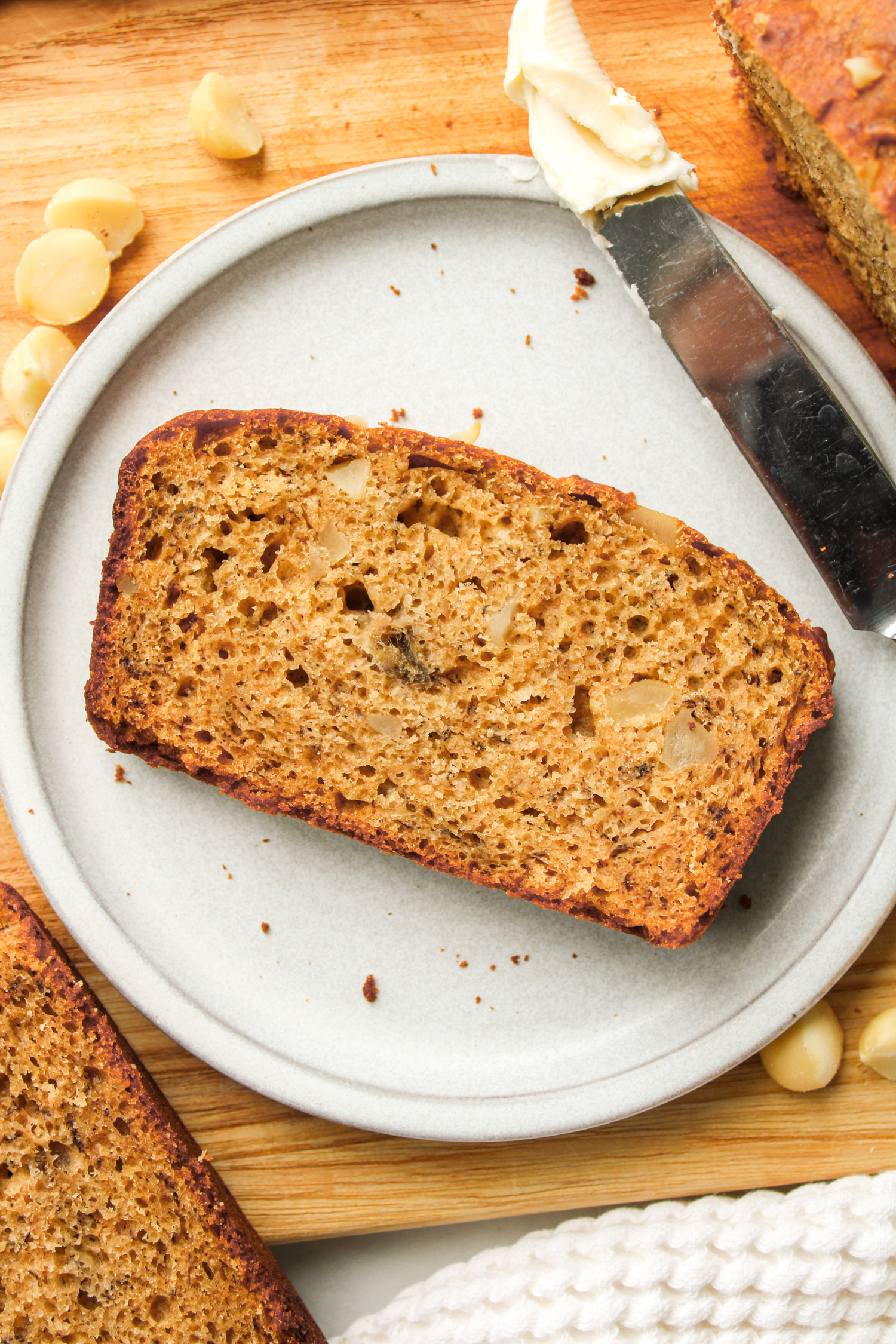 slice of macadamia banana bread on a grey ceramic plate on top of a wooden cutting board