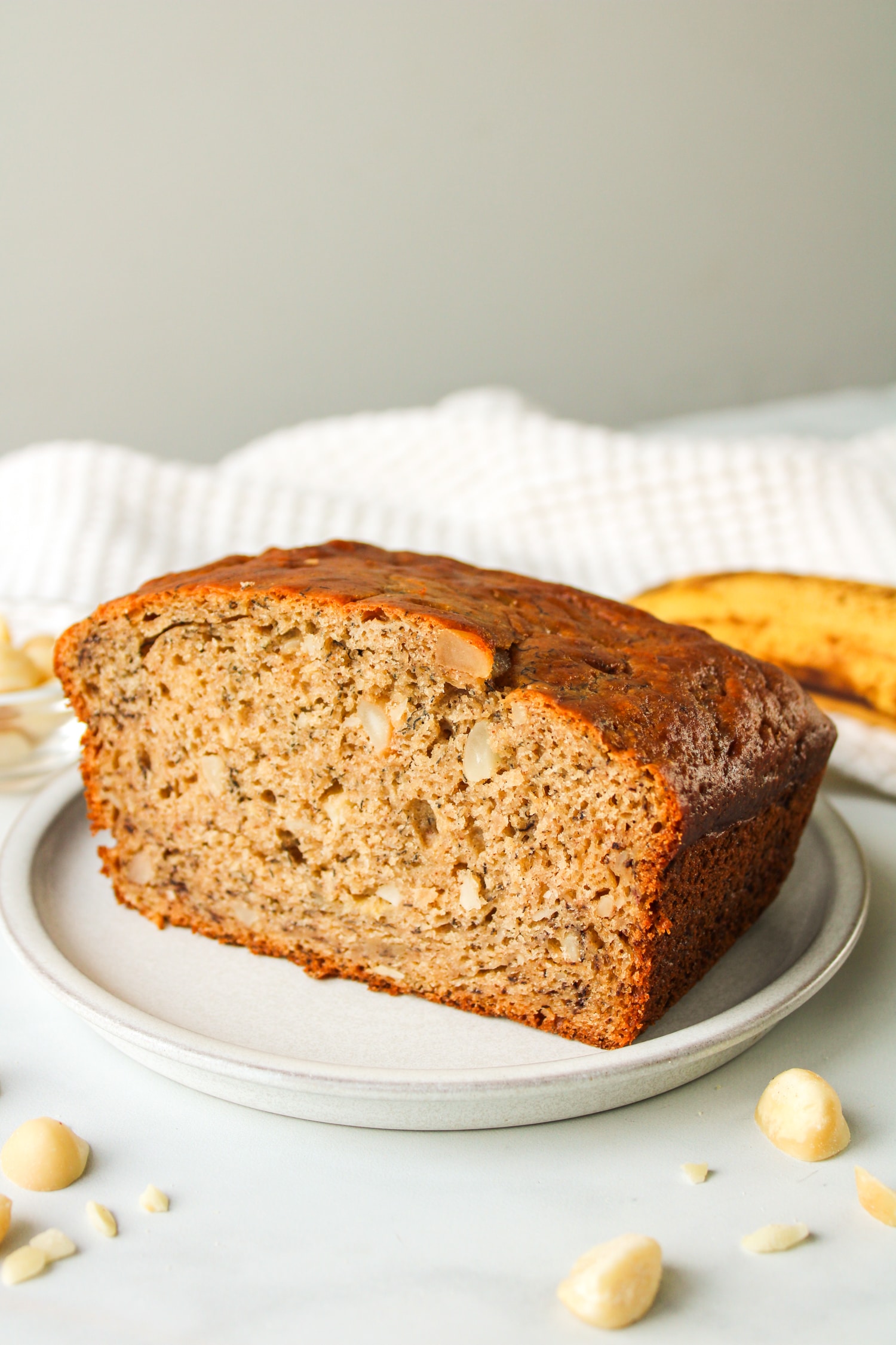 side shot of a sliced macadamia banana bread in a grey ceramic plate with a banana in the background