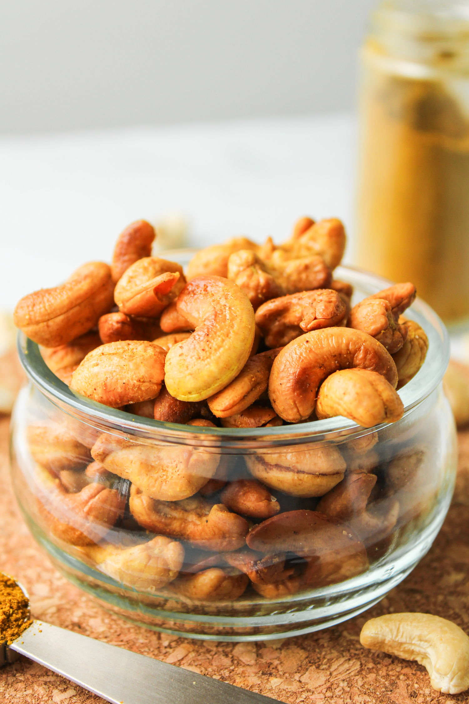 profile shot of roasted curry cashews in a glass bowl on top of a cork hot pad