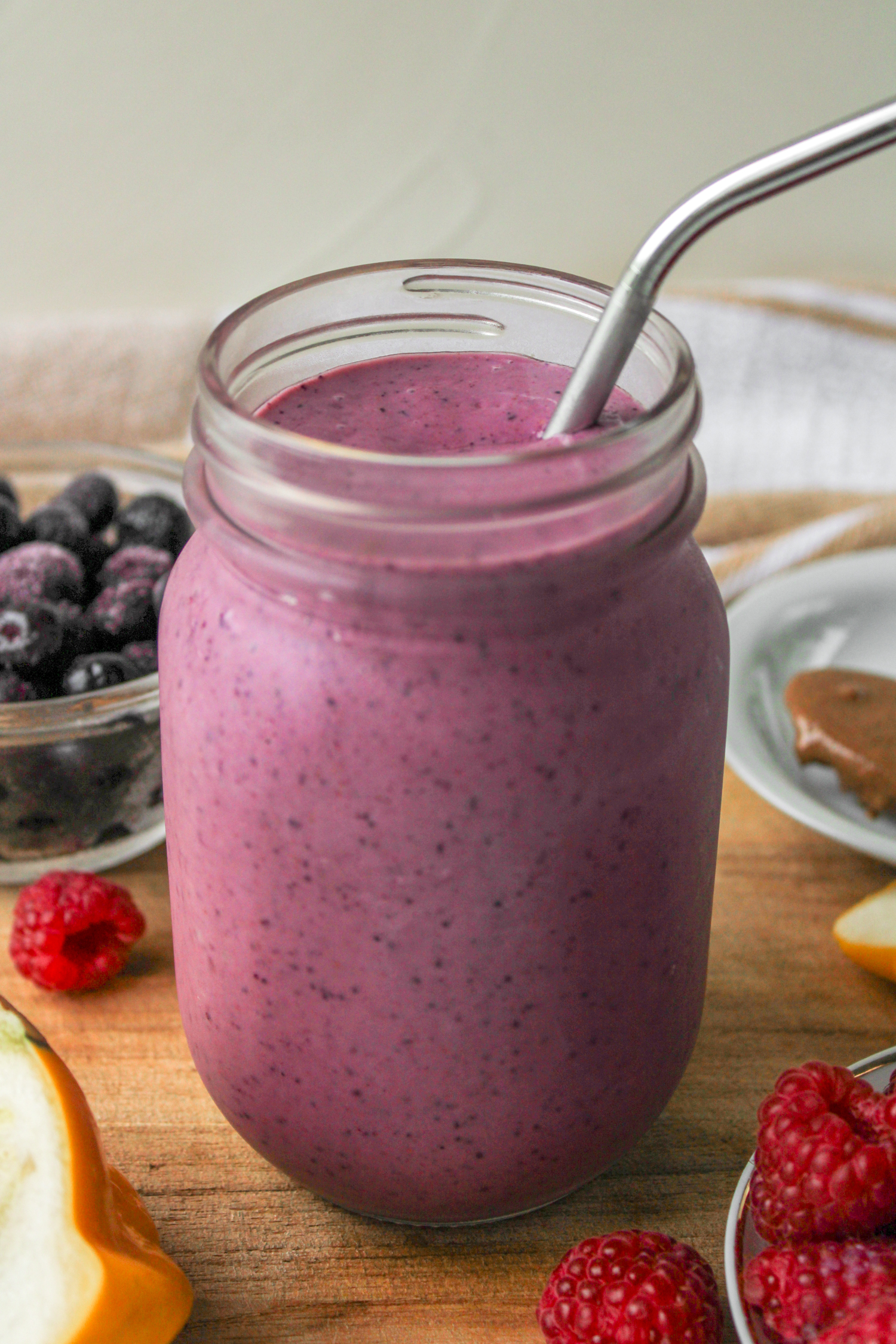 mixed berry smoothie in a glass mason jar with a metal straw on top of a wooden board