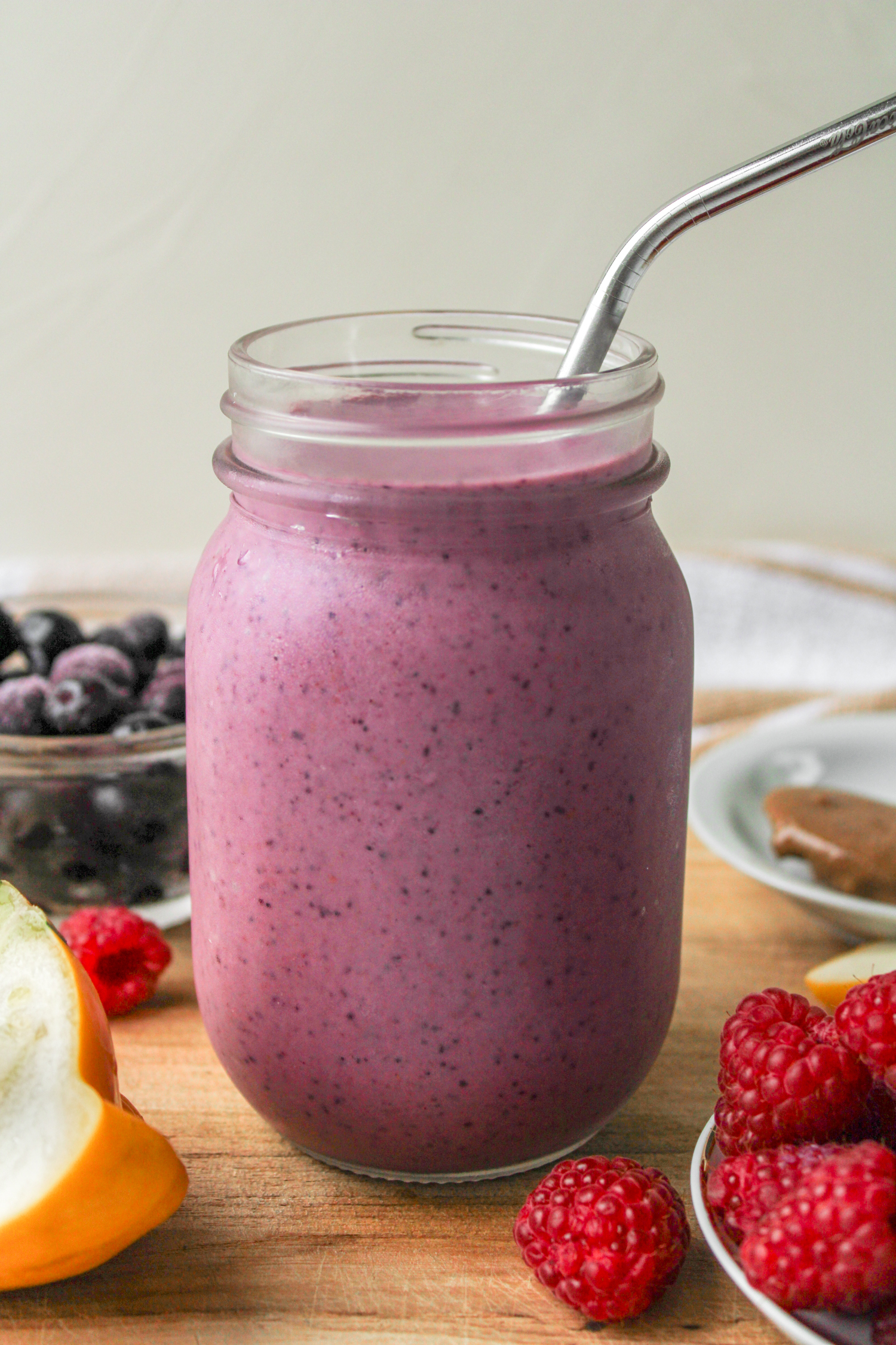 profile shot of raspberry blueberry smoothie in a glass mason jar with a metal straw on top of a wooden board