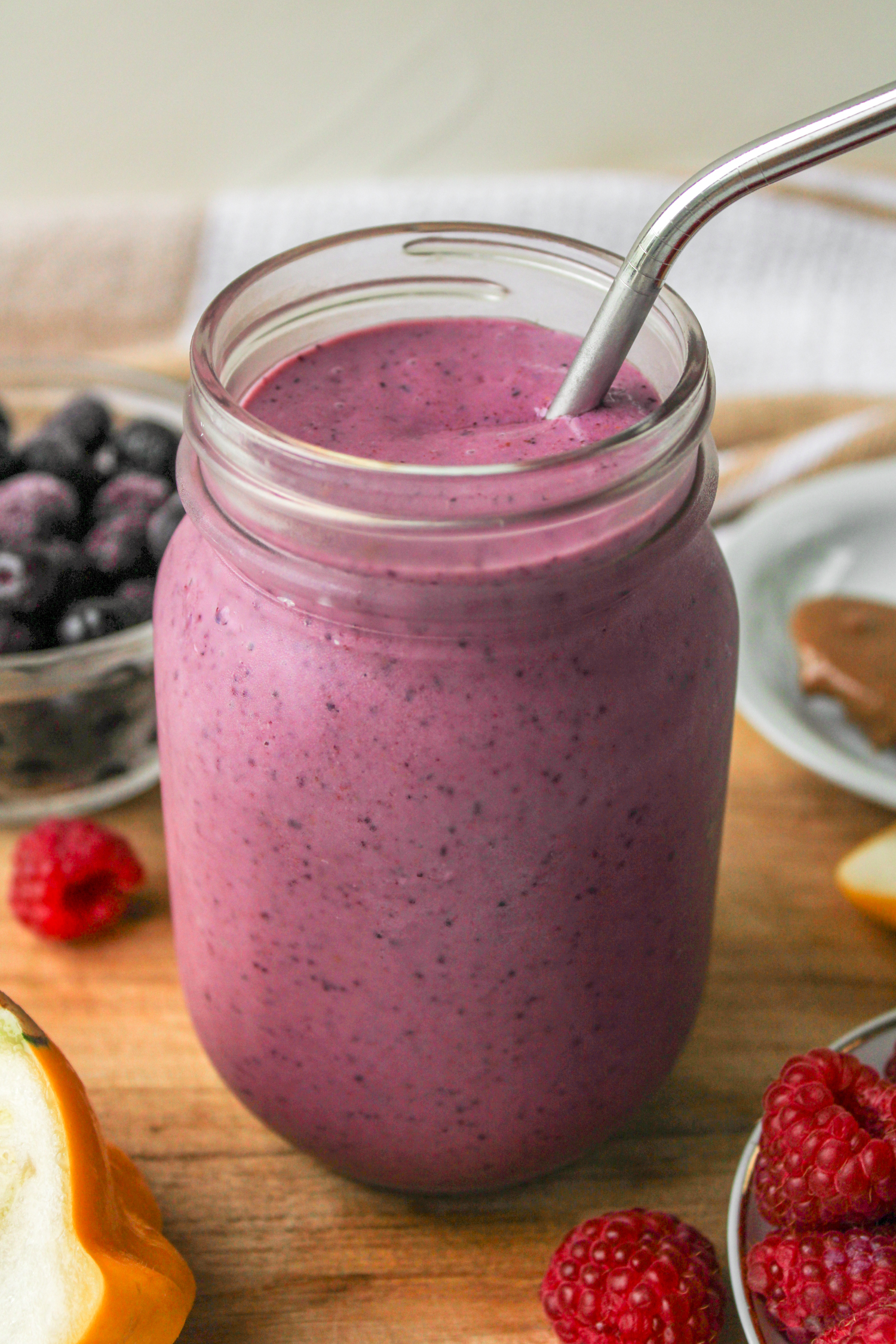 angled overhead shot of raspberry blueberry smoothie in a glass mason jar with a metal straw on top of a wooden board