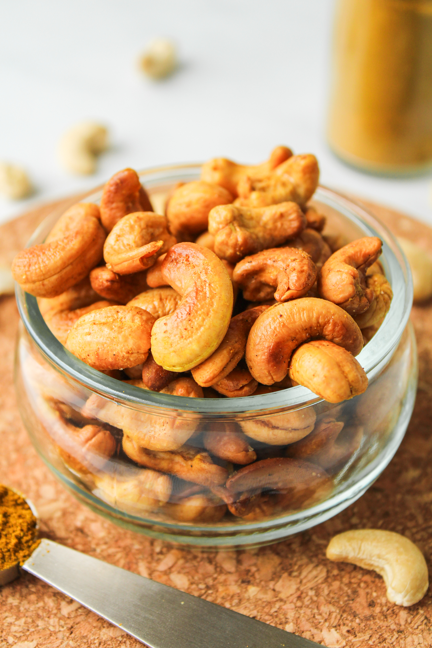 roasted curry cashews in a glass bowl on top of a cork hot pad