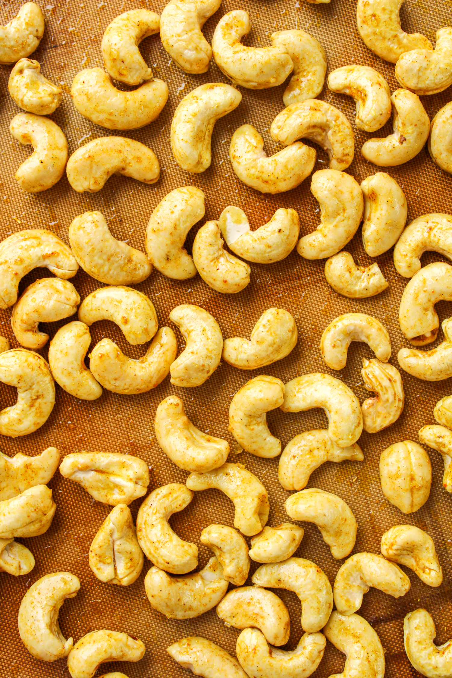 uncooked raw cashews with curry seasoning spread out on a baking tray