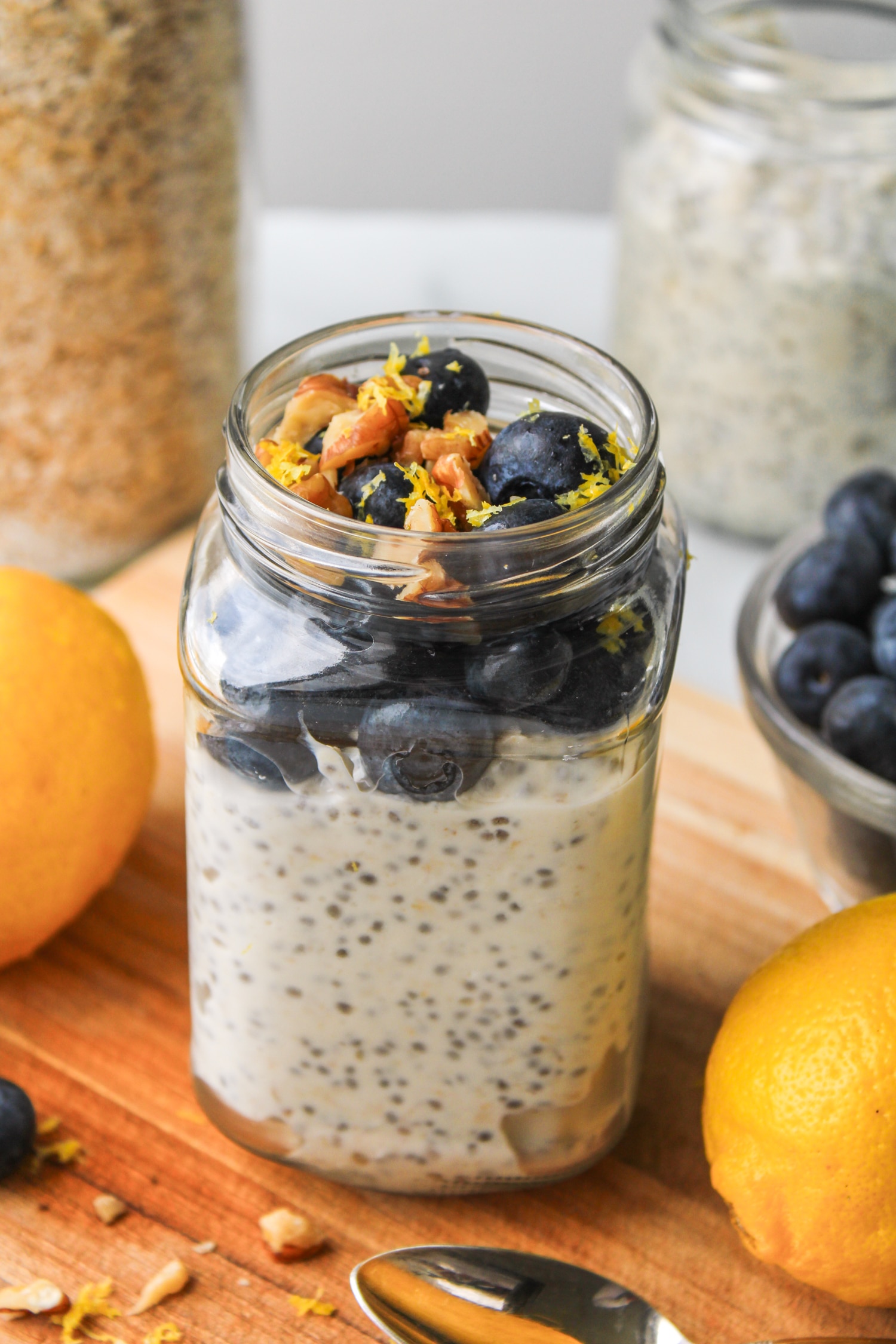 overhead shot of blueberry lemon overnight oats in a glass jar topped with fresh blueberries and lemon zest, on top of a wooden board