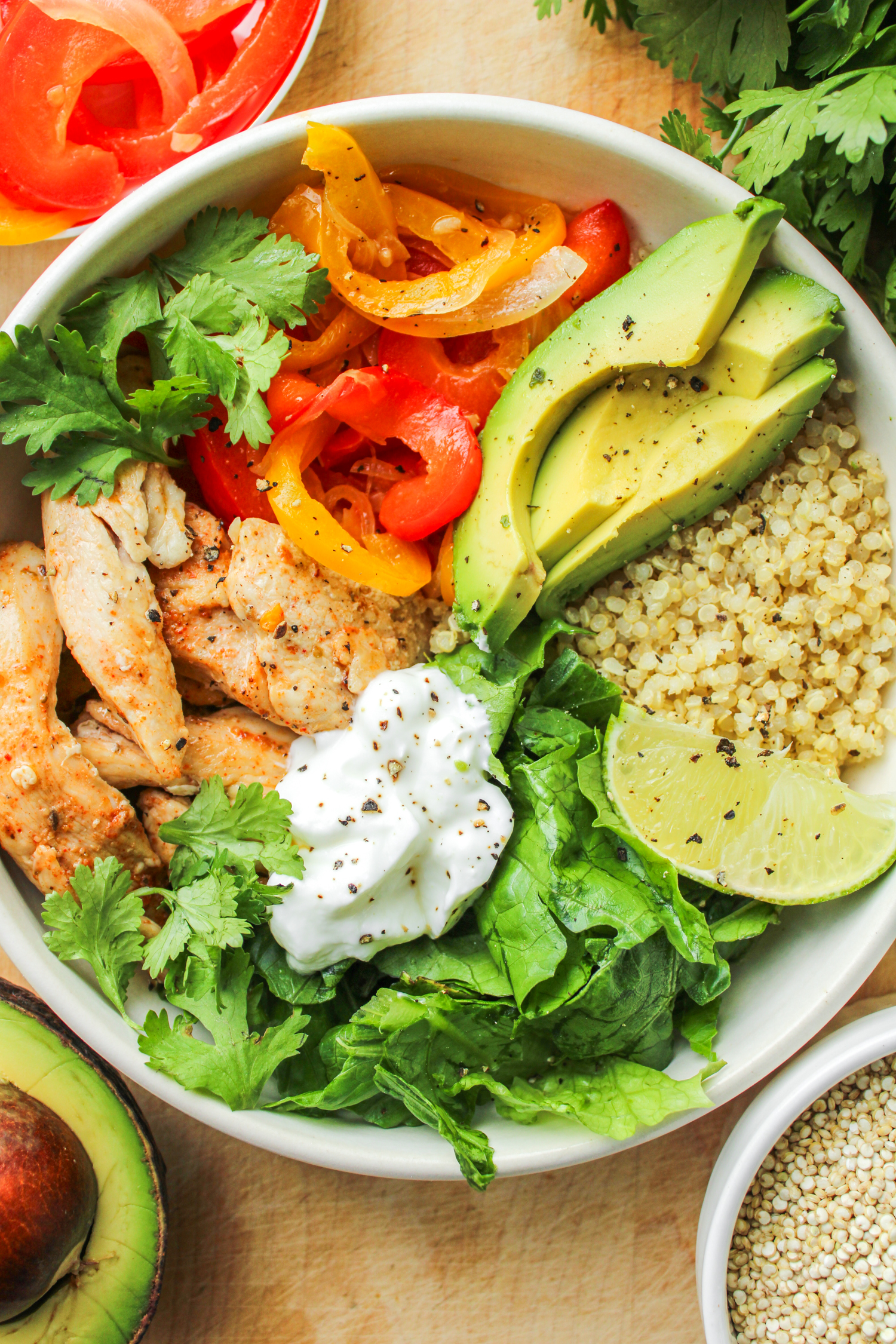 close up of chicken quinoa bowls in a white ceramic dish on top of a wooden cutting board