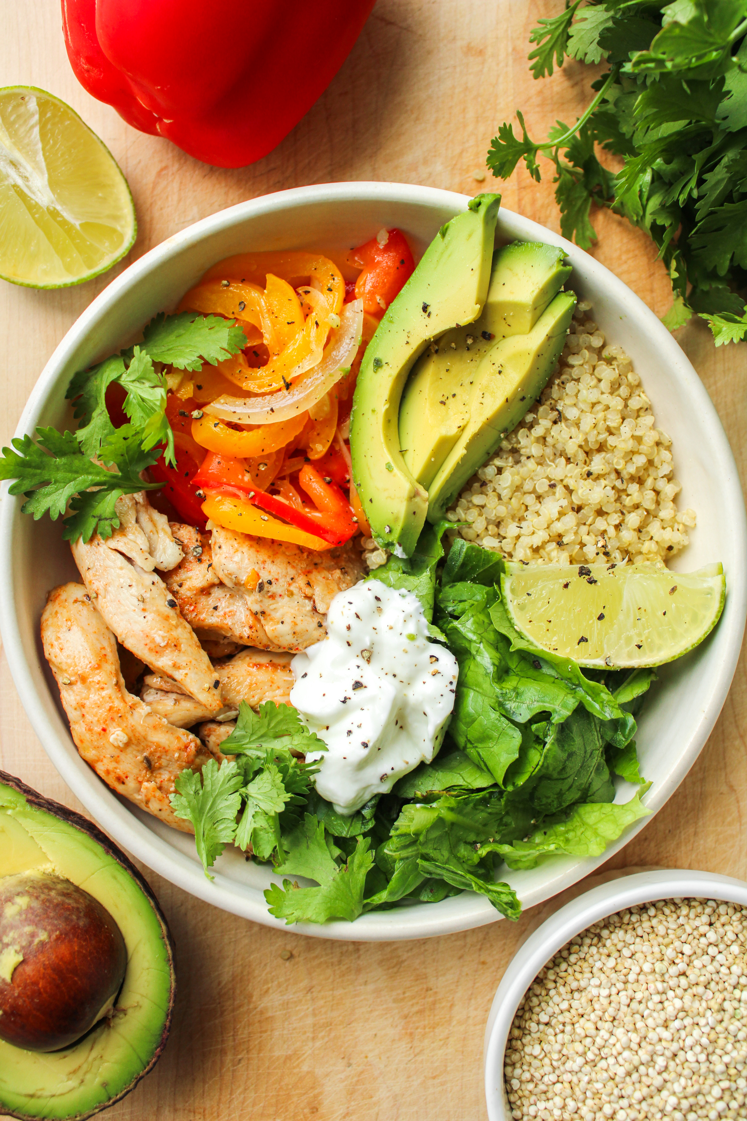 chicken quinoa bowls in a white ceramic dish on top of a wooden cutting board