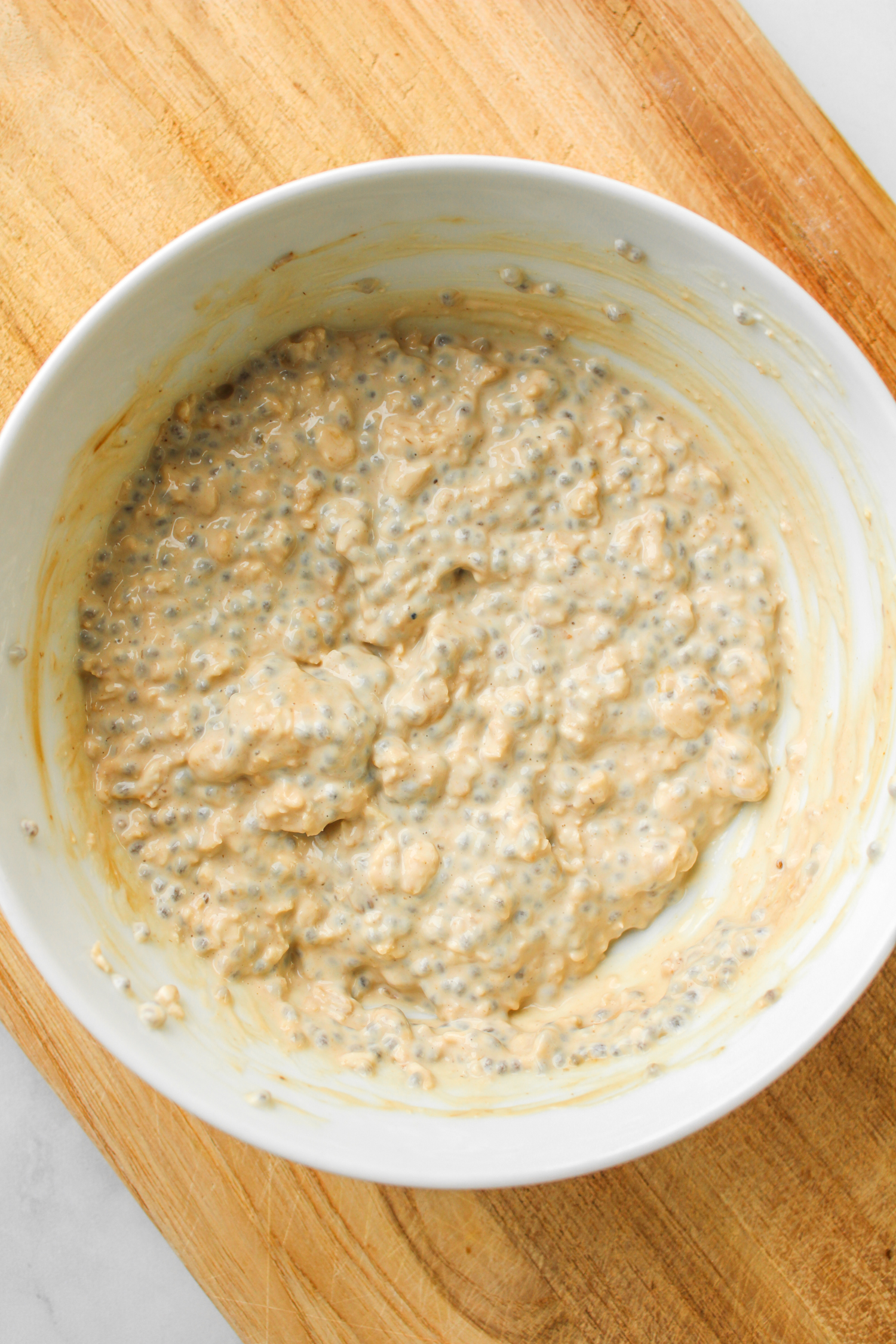 espresso powder mixed into overnight oats in a white ceramic bowl on top of a wooden cutting board