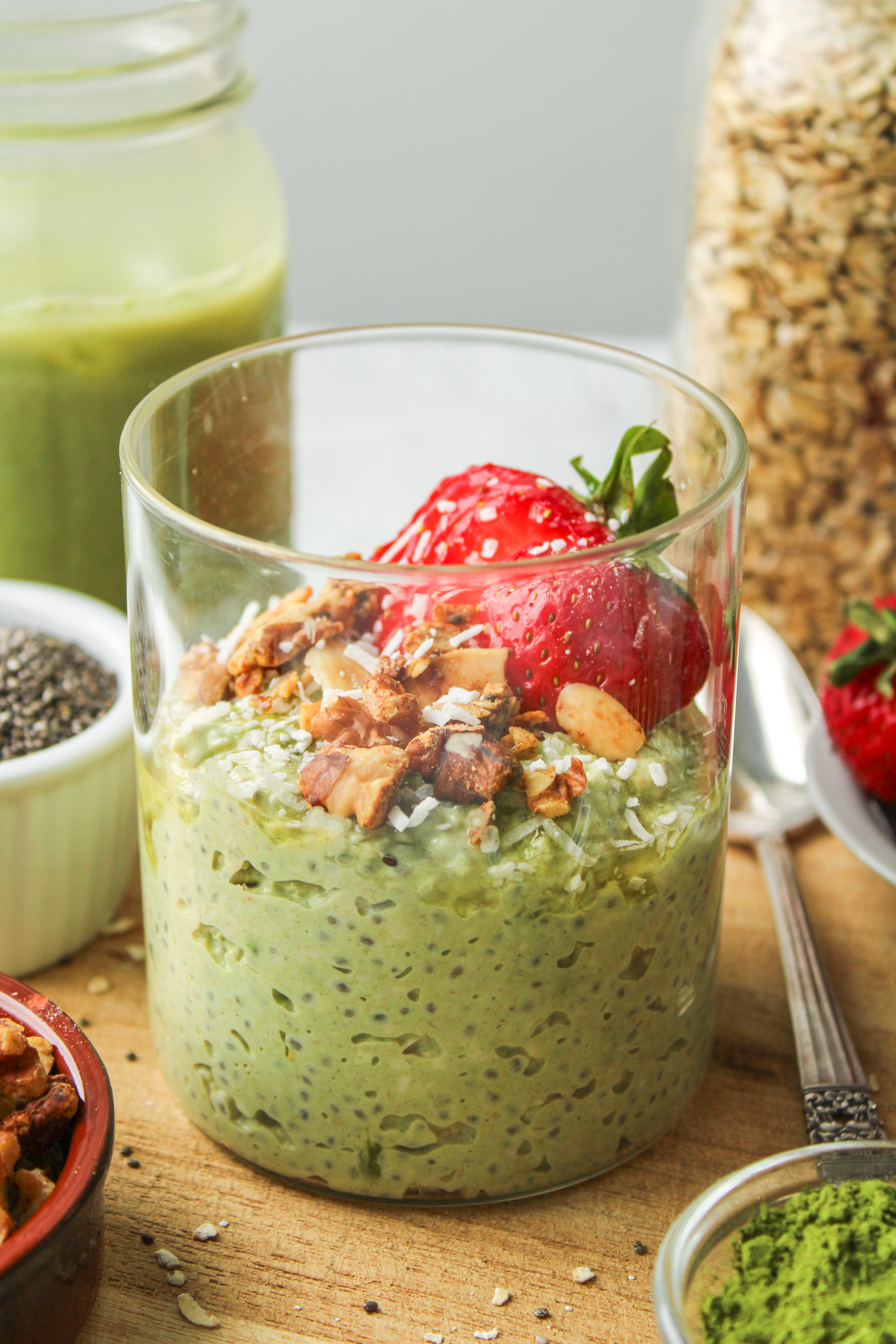 green tea overnight oats in a glass jar topped with strawberries and granola on top of a wooden cutting board