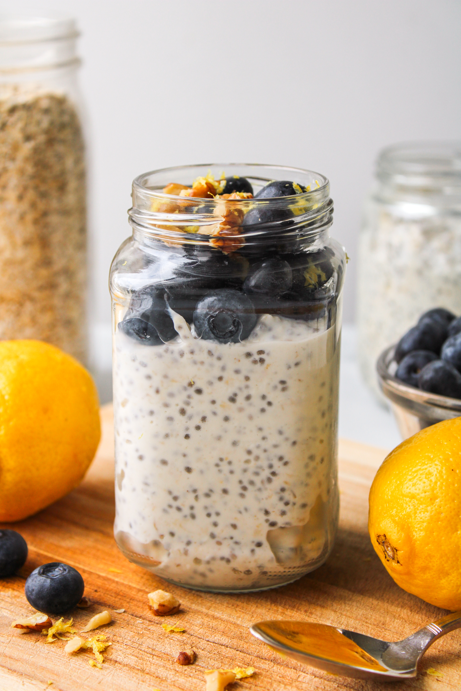 overhead shot of lemon blueberry oats in a glass jar topped with fresh blueberries and lemon zest, on top of a wooden board