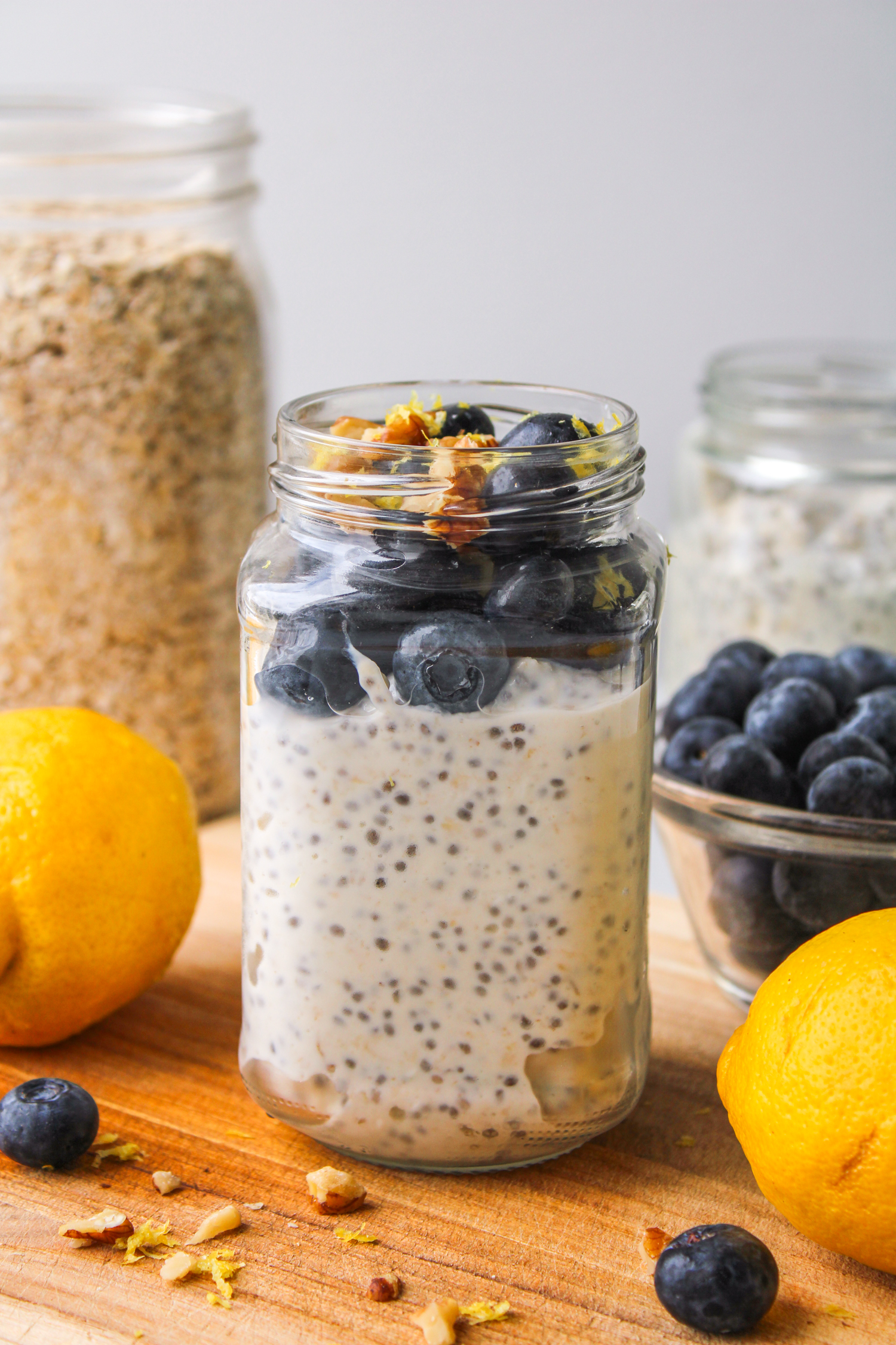 lemon blueberry overnight oats in a glass jar topped with fresh blueberries and lemon zest, on top of a wooden board