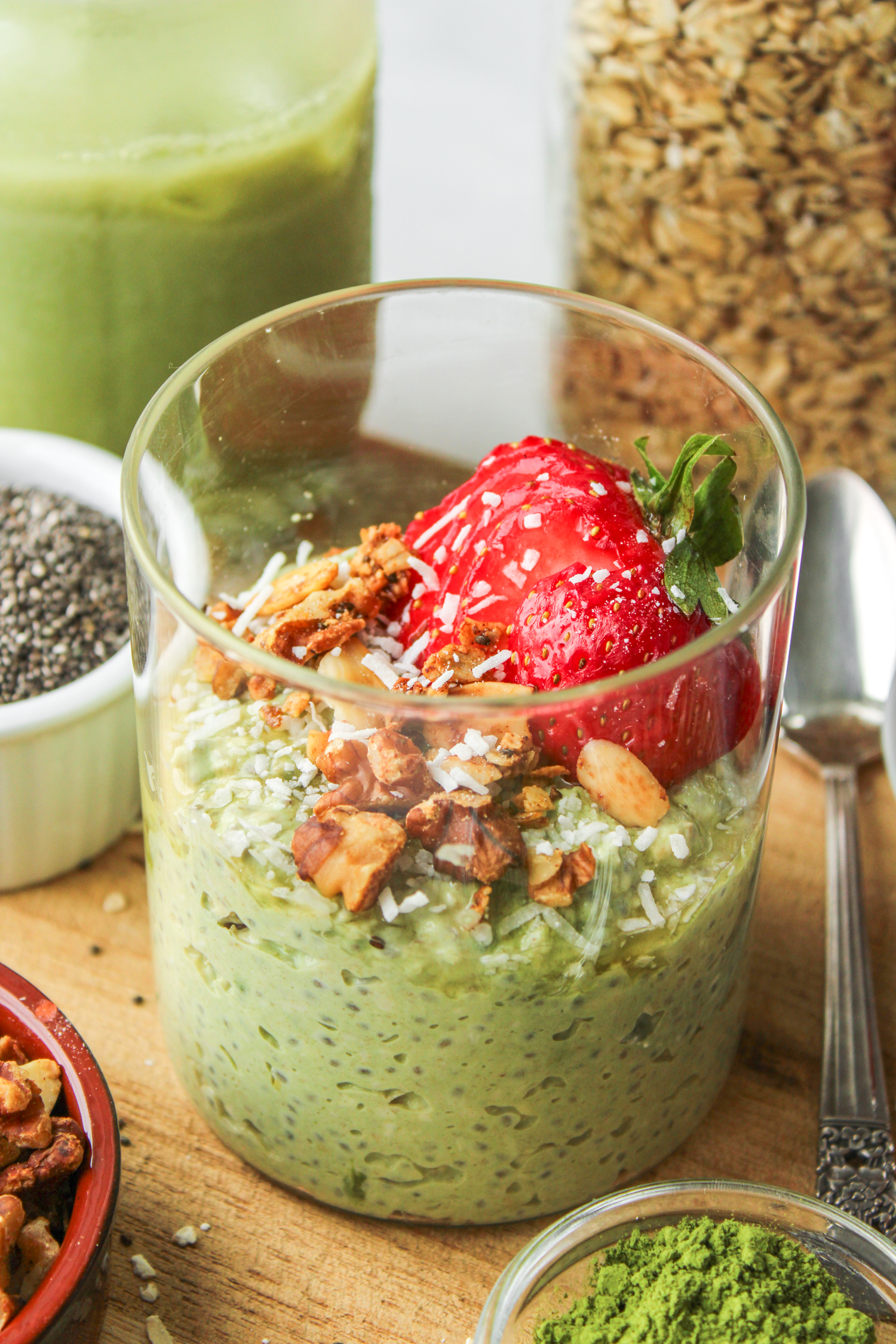 overhead shot of matcha oats in a glass jar topped with strawberries and granola on top of a wooden cutting board