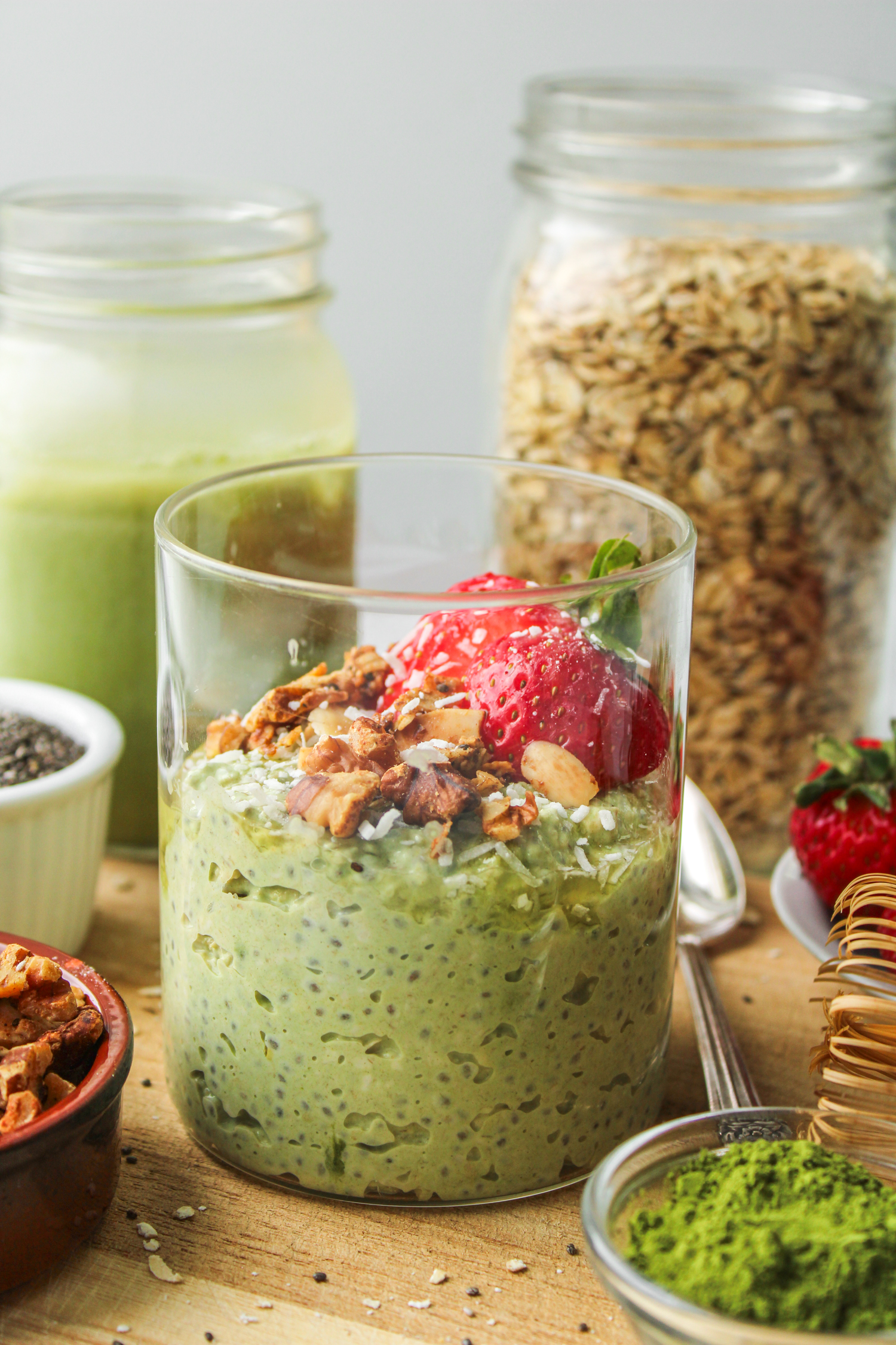 matcha overnight oats in a glass jar topped with strawberries and granola on top of a wooden cutting board