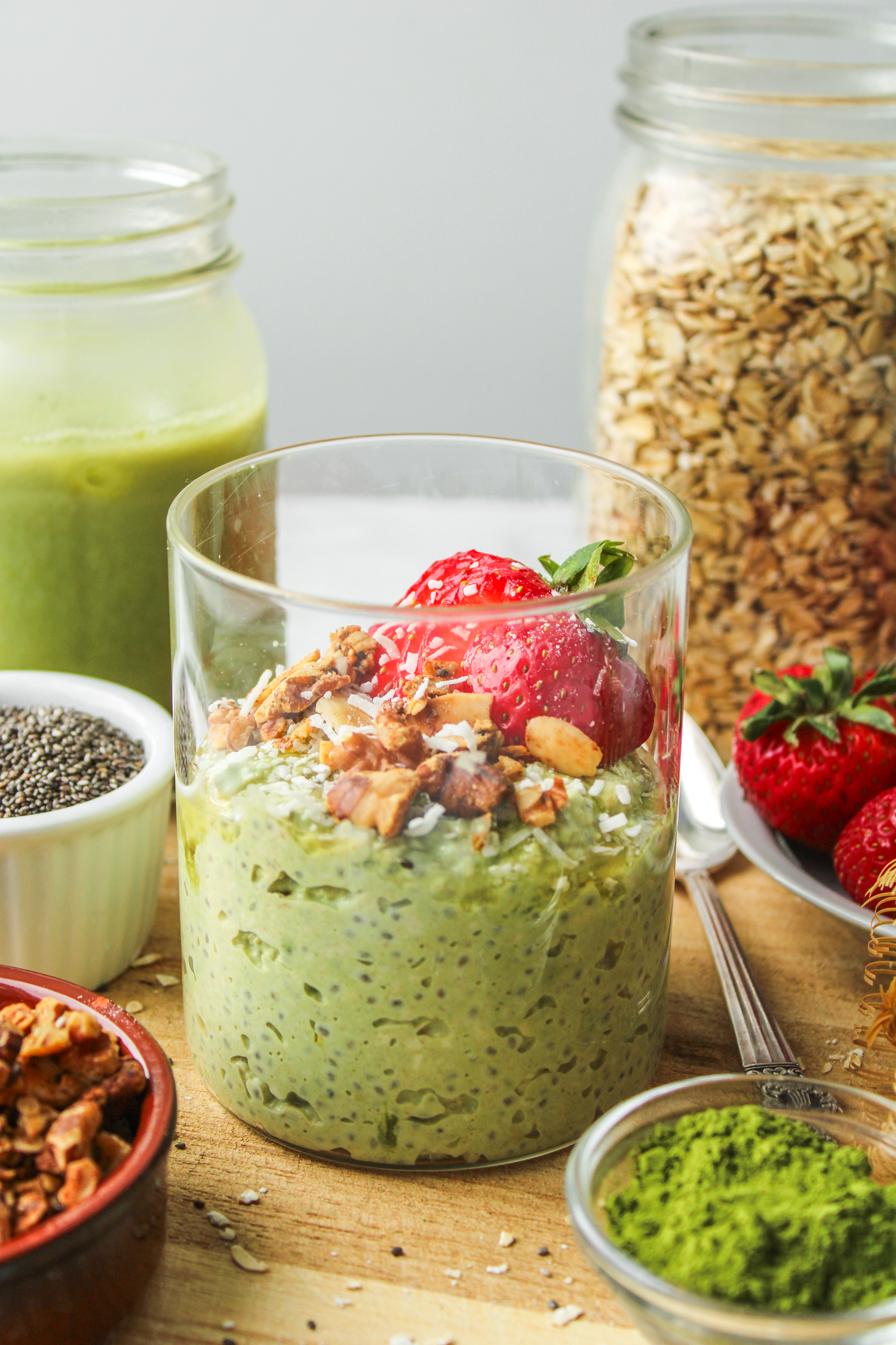 profile shot of matcha powder oats in a glass jar topped with strawberries and granola on top of a wooden cutting board