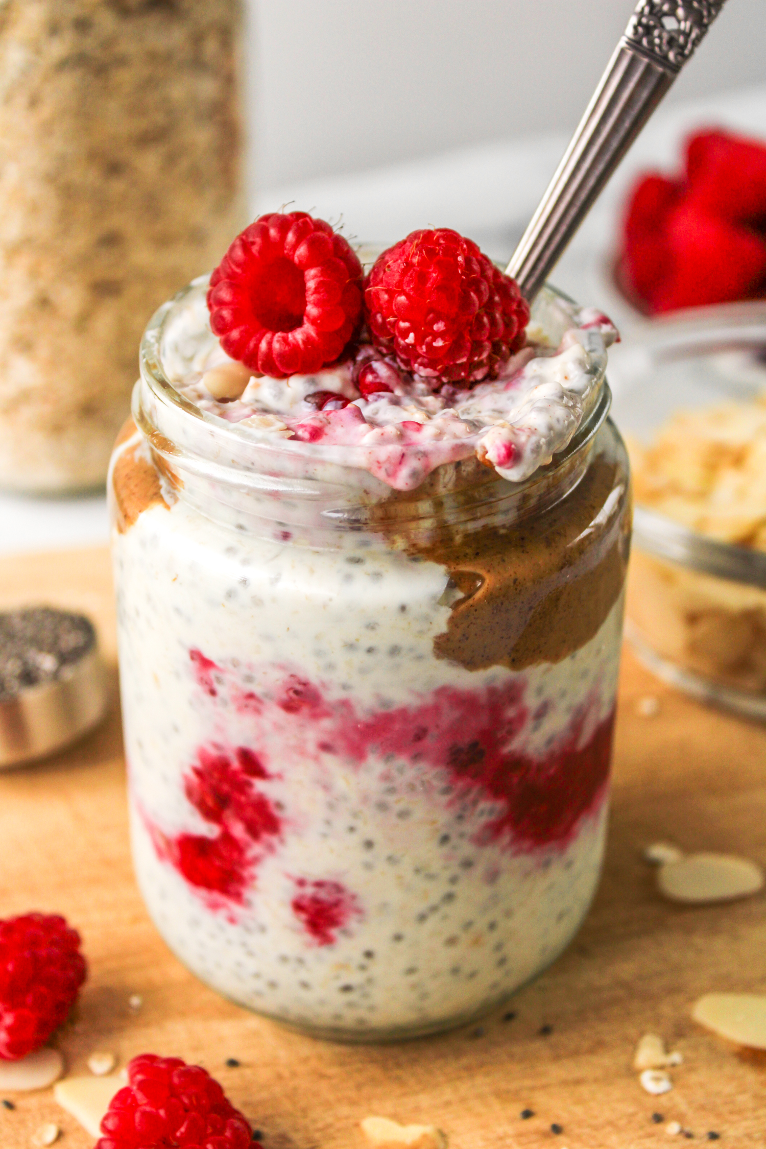 mixed overnight oats layered in a glass jar topped with raspberries, almond butter and sliced almonds