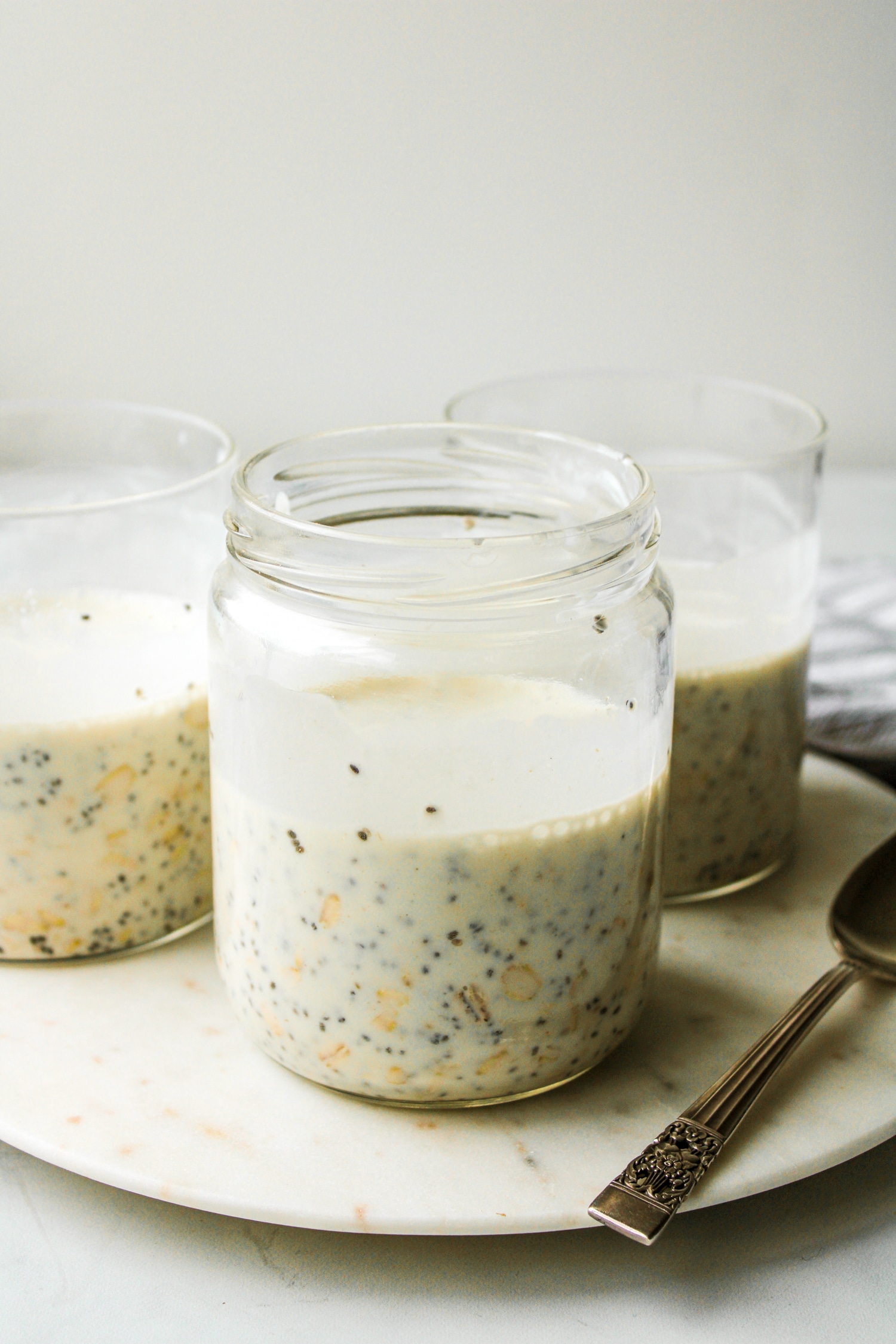 three overnight oats base recipe each in glass containers on top of a marble serving platter