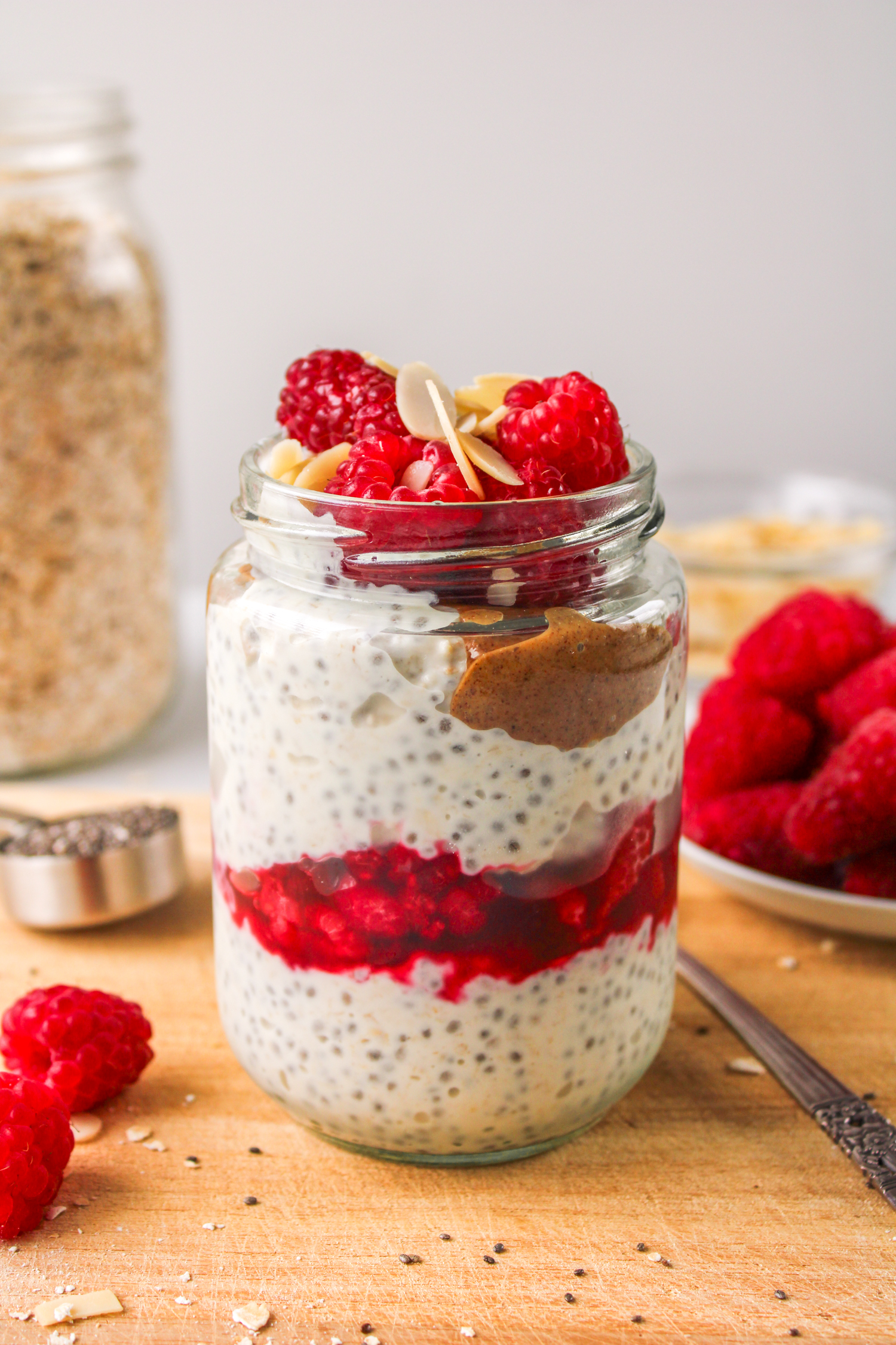 almond overnight oats layered in a glass jar topped with raspberries and sliced almonds