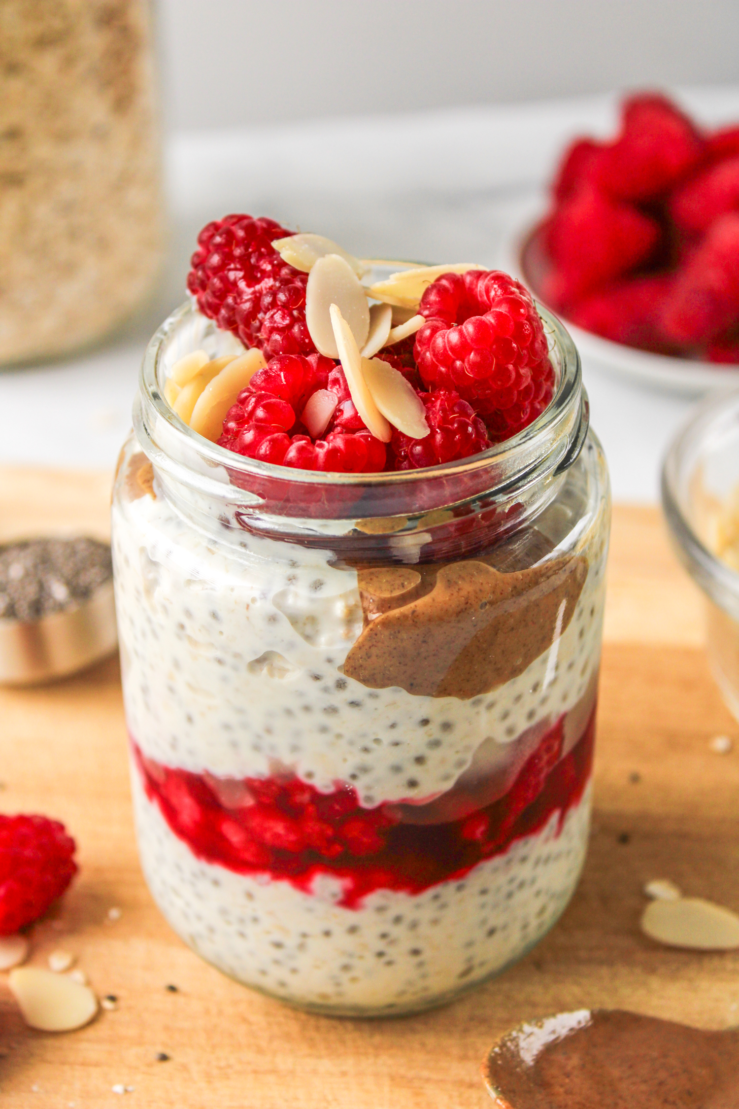 close up of raspberry overnight oats layered in a glass jar topped with raspberries and sliced almonds