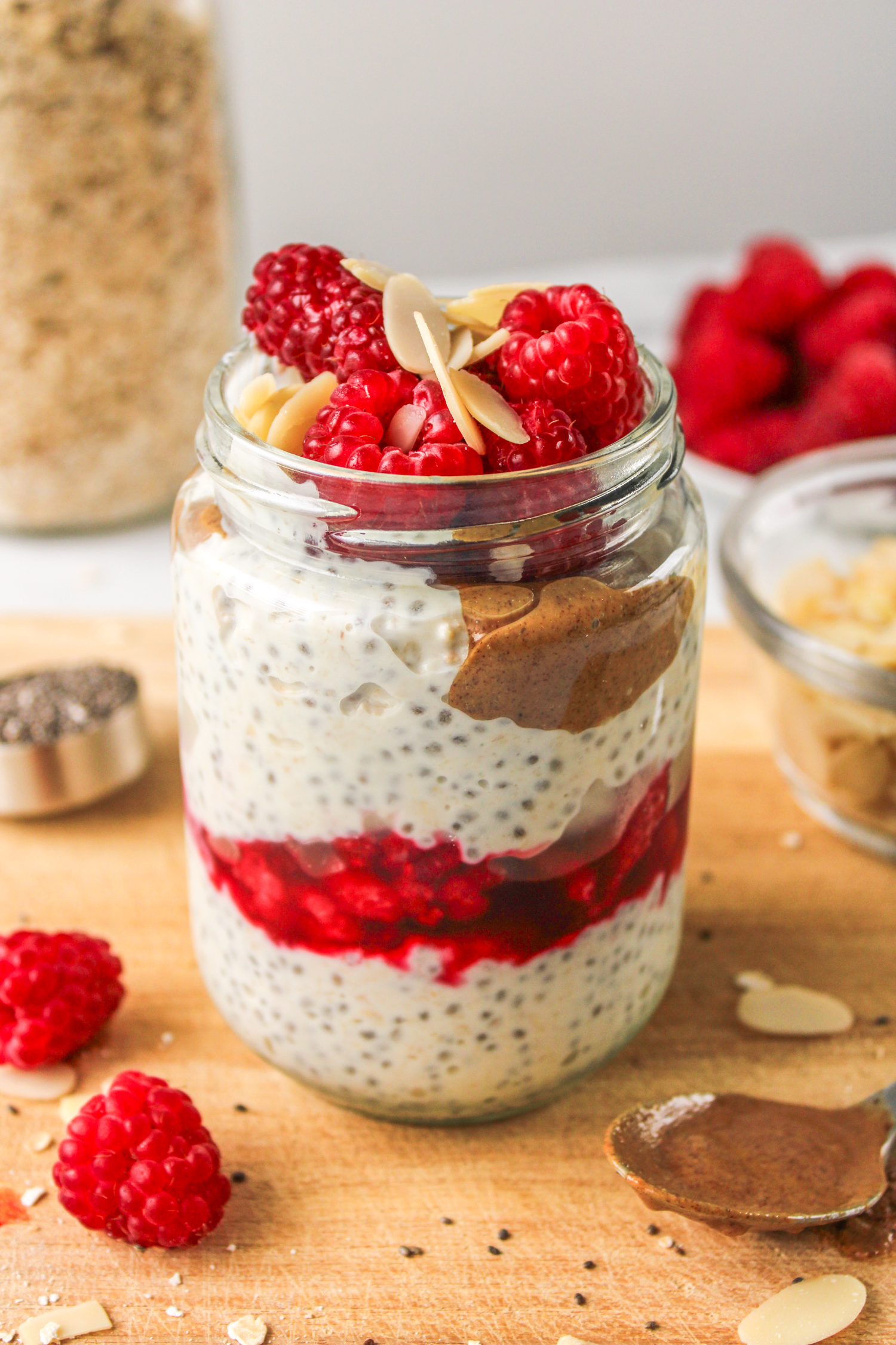 raspberry overnight oats layered in a glass jar topped with raspberries and sliced almonds