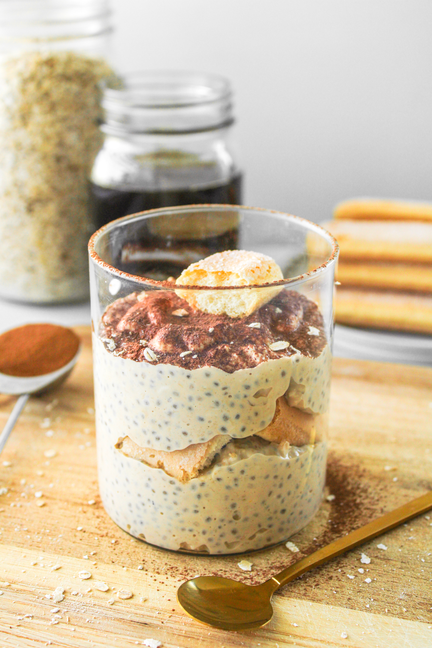 tiramisu overnight oats topped with cocoa powder and a ladyfinger cookie in glass jar on top of wooden board