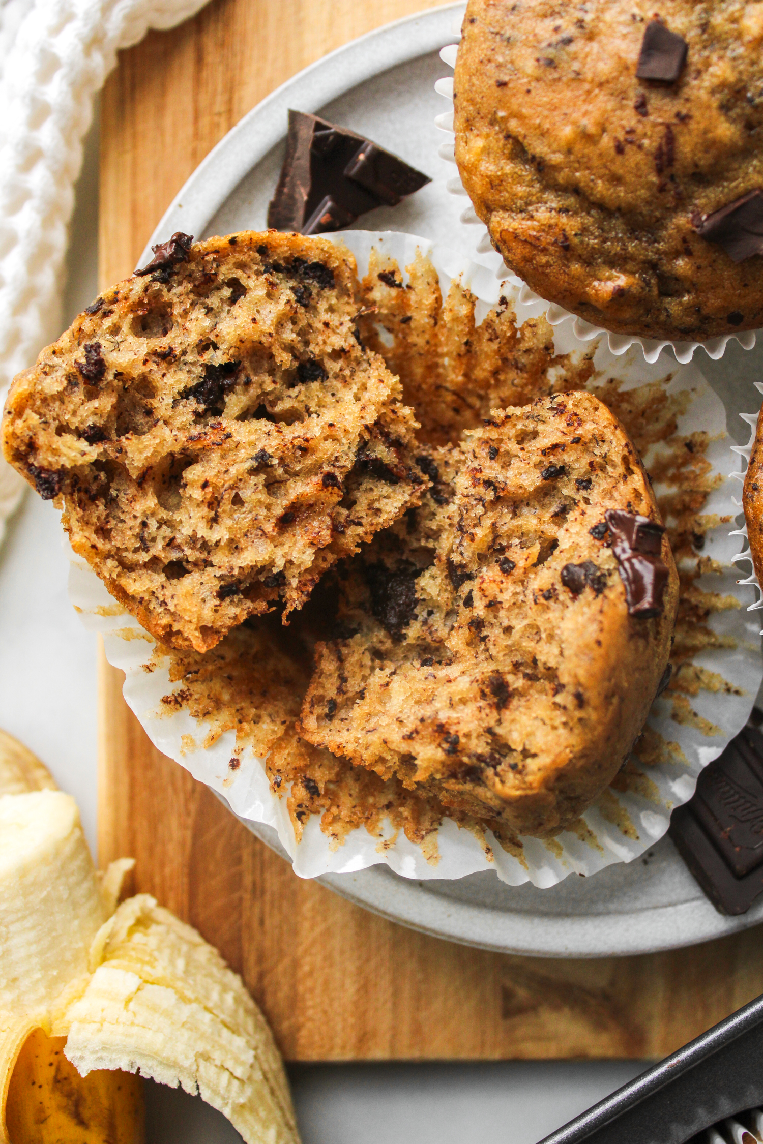 overhead shot of a banana chocolate chunk muffin pulled apart on a muffin liner with more muffins in the background