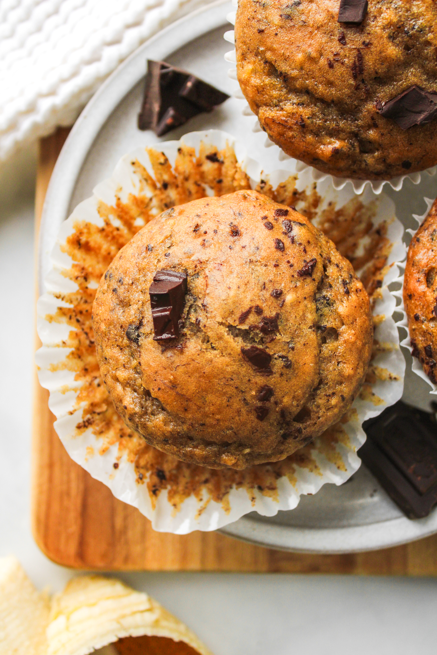 overhead shot of a banana chocolate chunk muffin on a grey ceramic plate with more muffins in the background