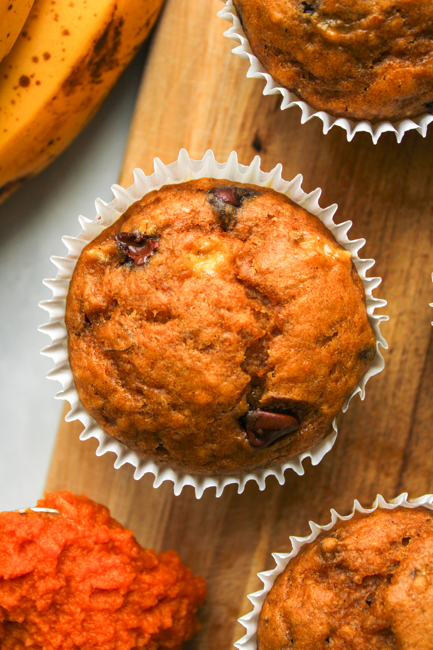 one pumpkin banana bread muffin in white paper muffin liners on a wooden board