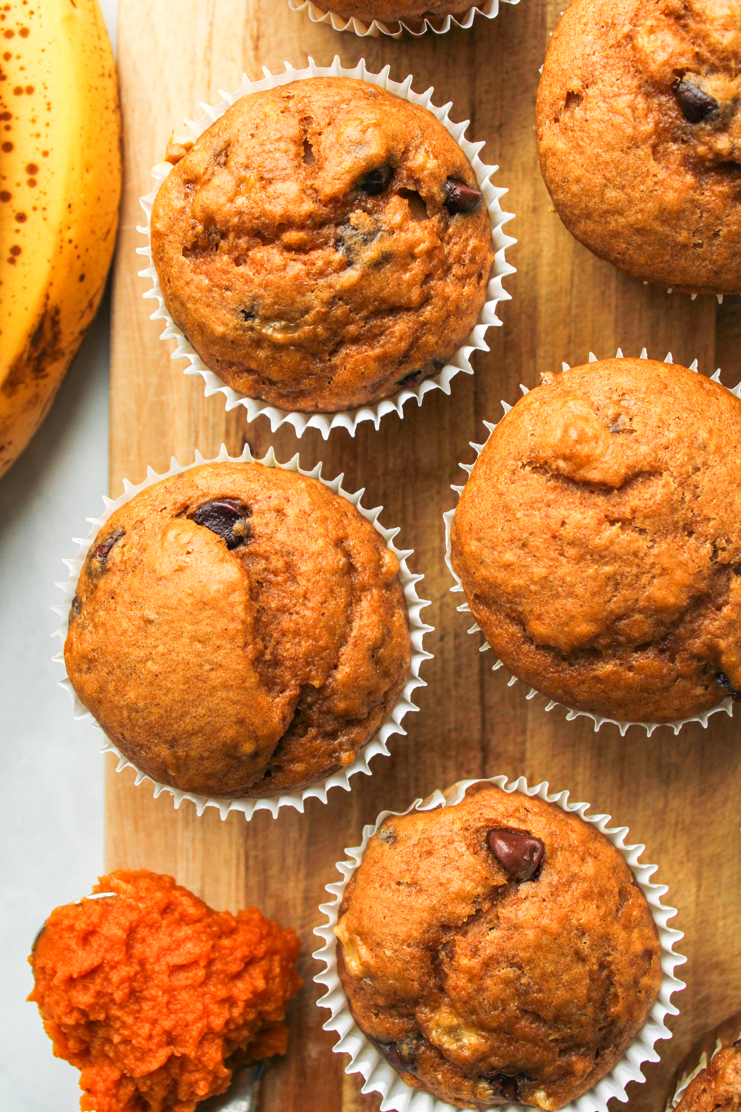 pumpkin banana bread muffins in white paper muffin liners on a wooden board