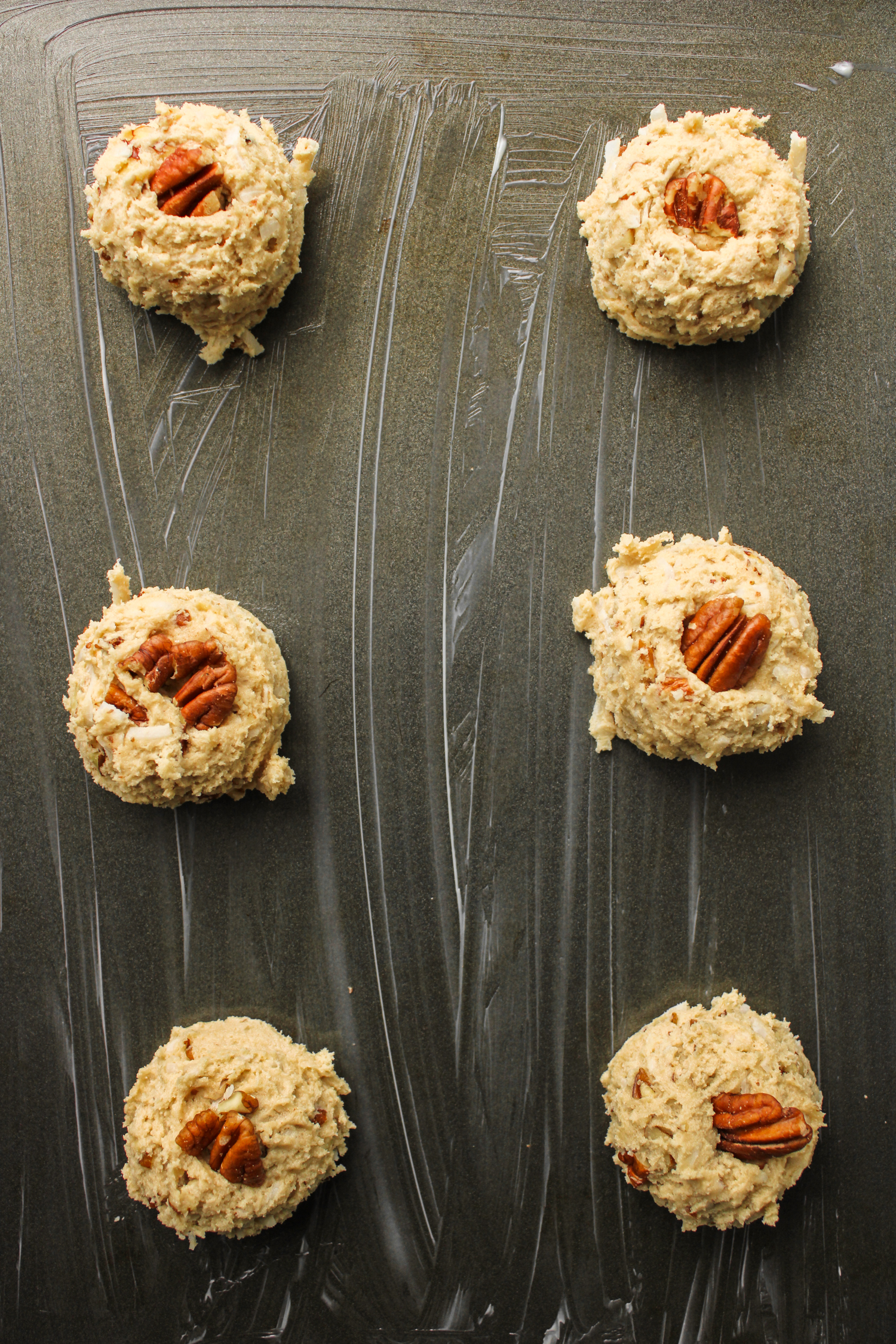 cookie dough balls with coconut and pecans on a greased baking tray