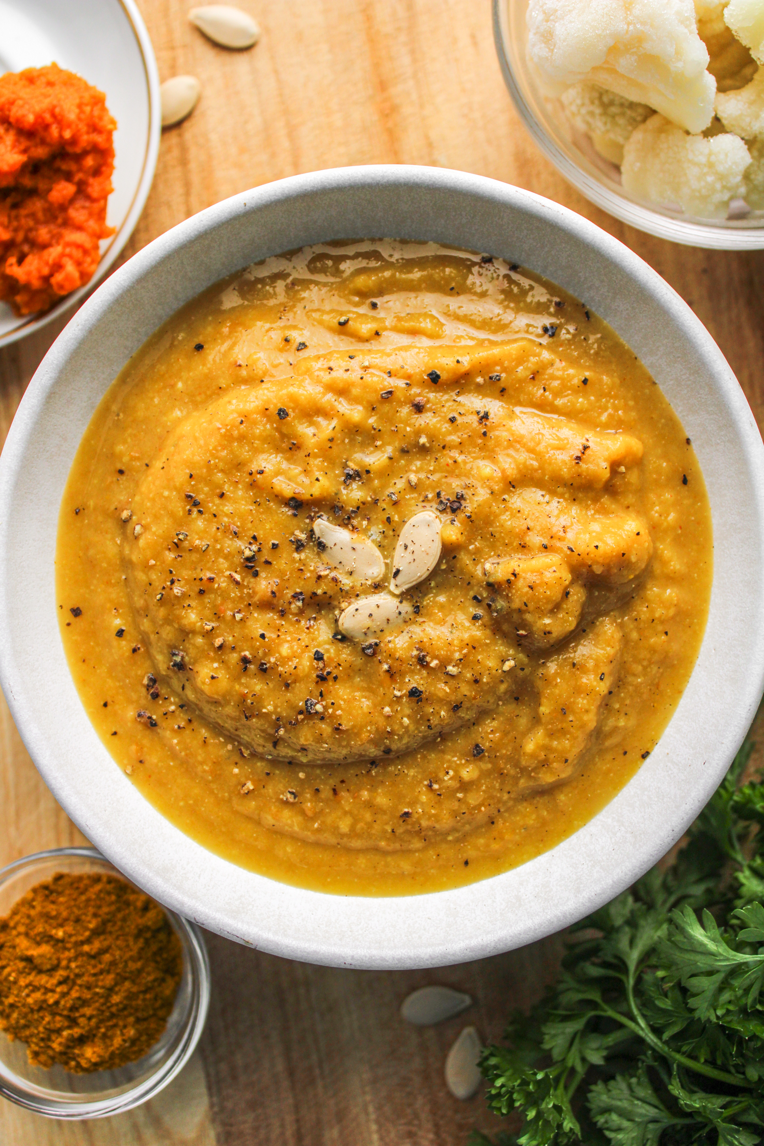 cauliflower pumpkin soup in white ceramic bowl topped with pumpkin seeds and ingredients surrounding it