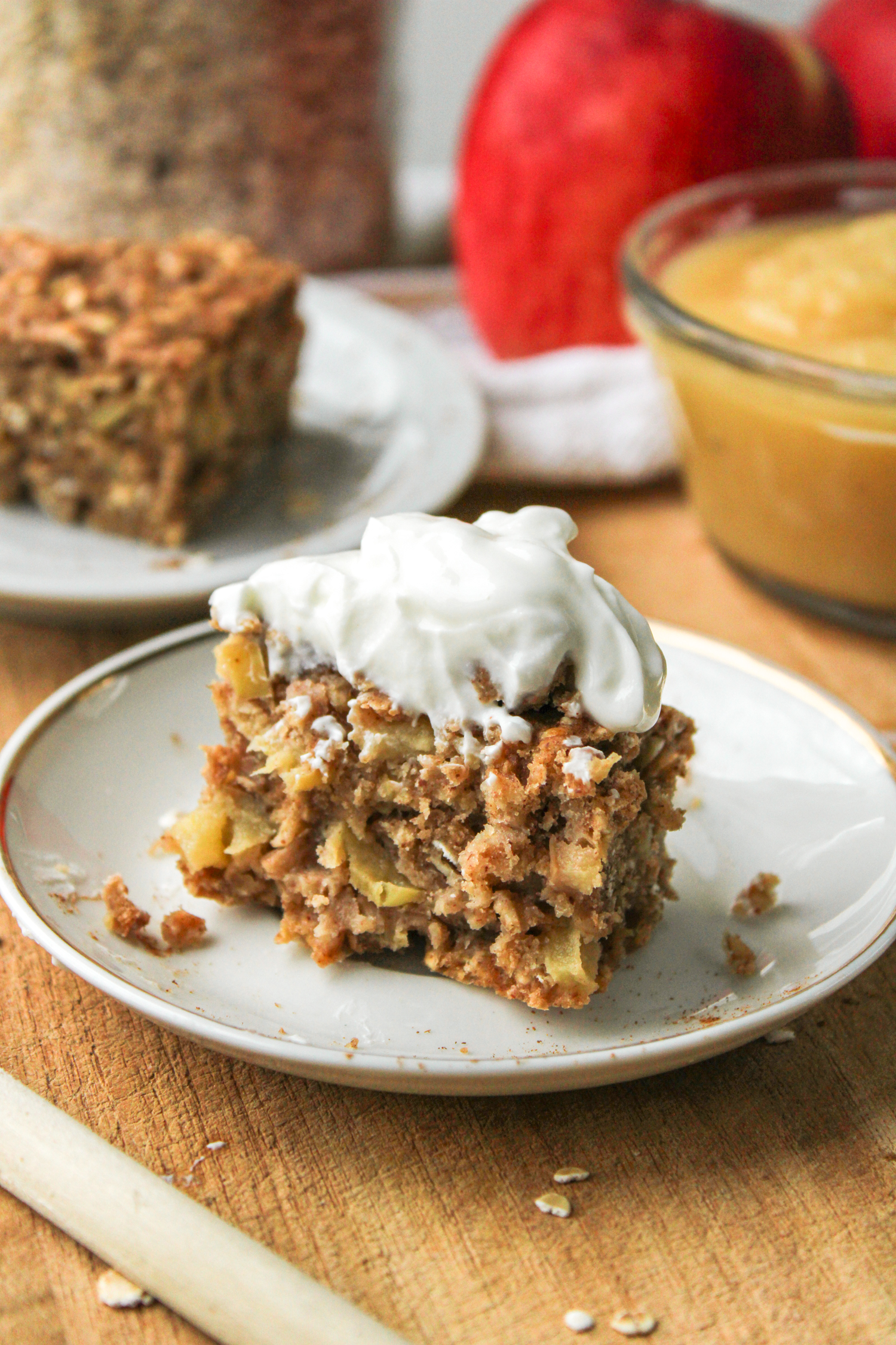 a baked oatmeal bar with yogurt on top of it on a small white ceramic plate with ingredients in the background