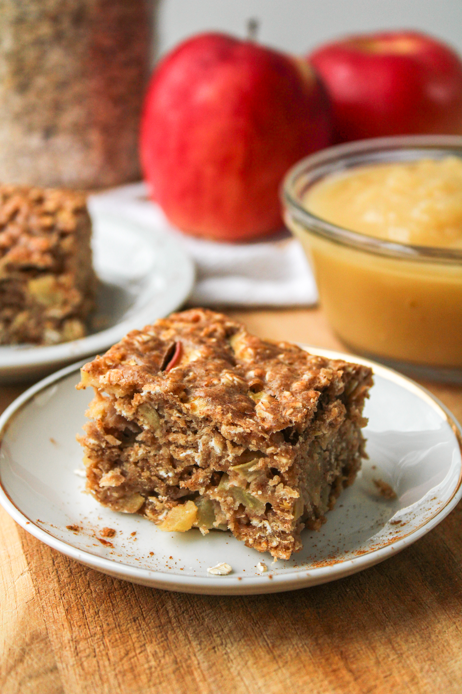 a breakfast apple oatmeal bar on a small white ceramic plate with ingredients in the background