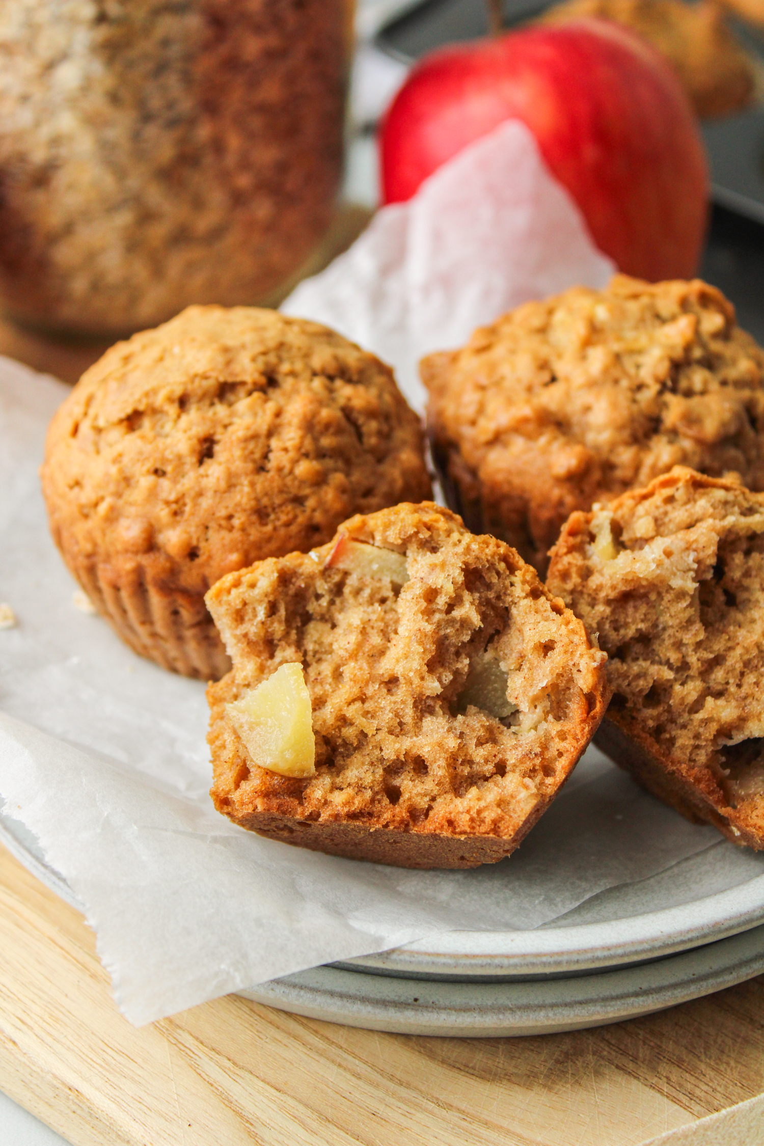 a pulled apart apple oatmeal muffins on stacked white ceramic plates with other muffins surrounding it