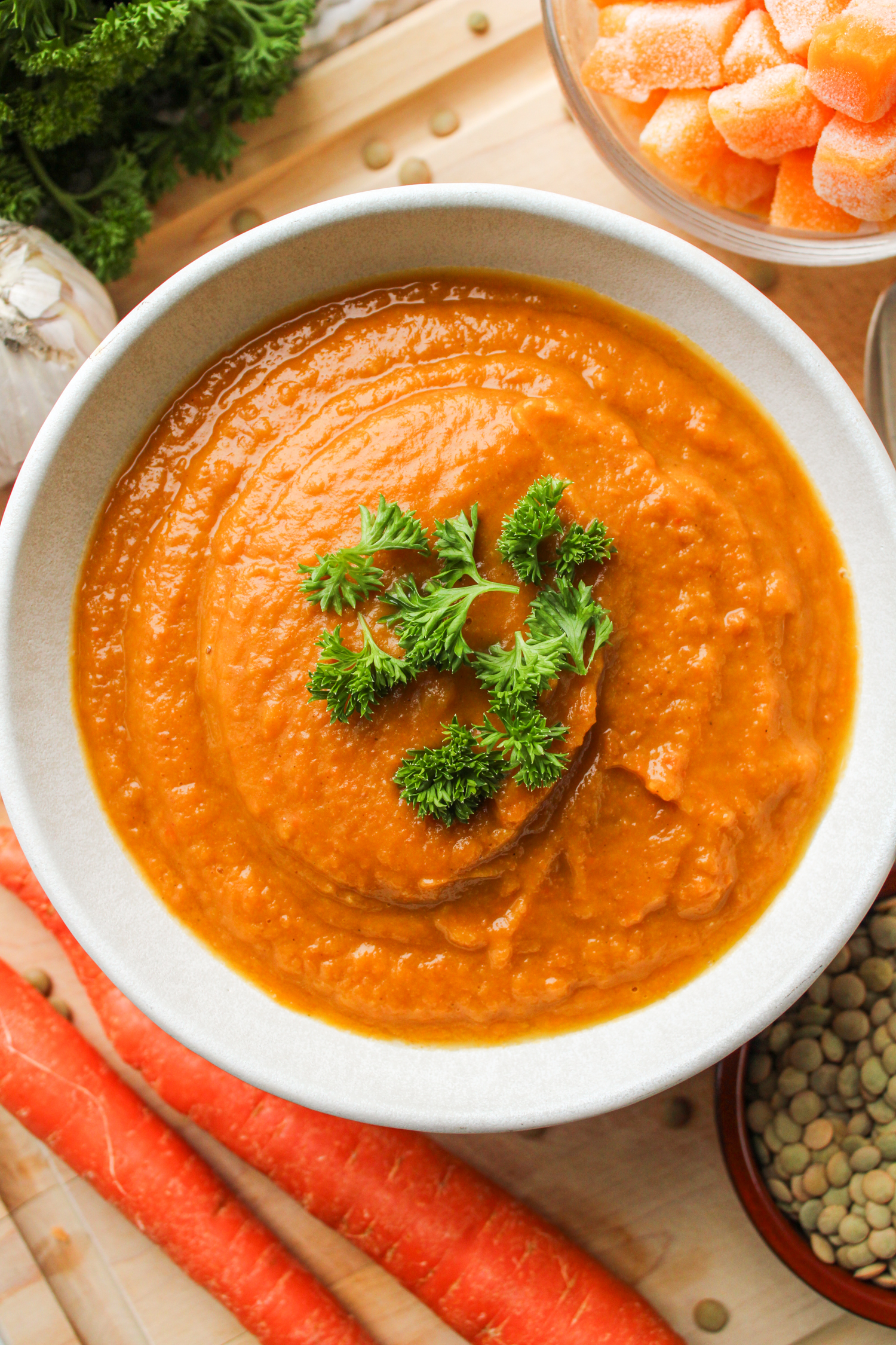 butternut squash and carrot soup topped with green parsley, in a white ceramic bowl on top of a wooden cutting board