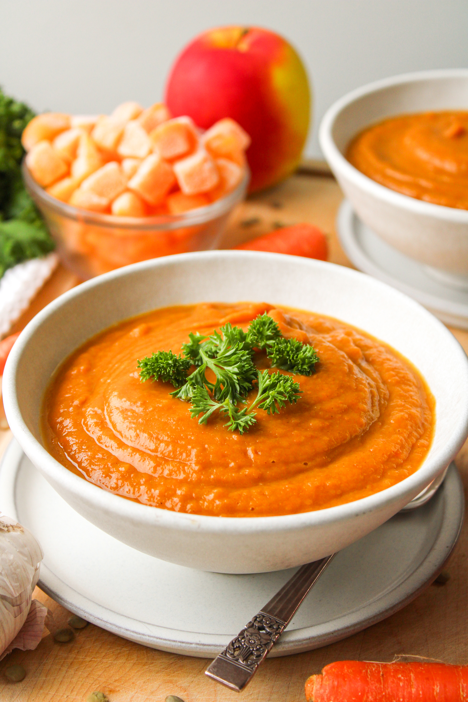 profile shot of squash and carrot soup topped with green parsley, in a white ceramic bowl on top of a white ceramic plate