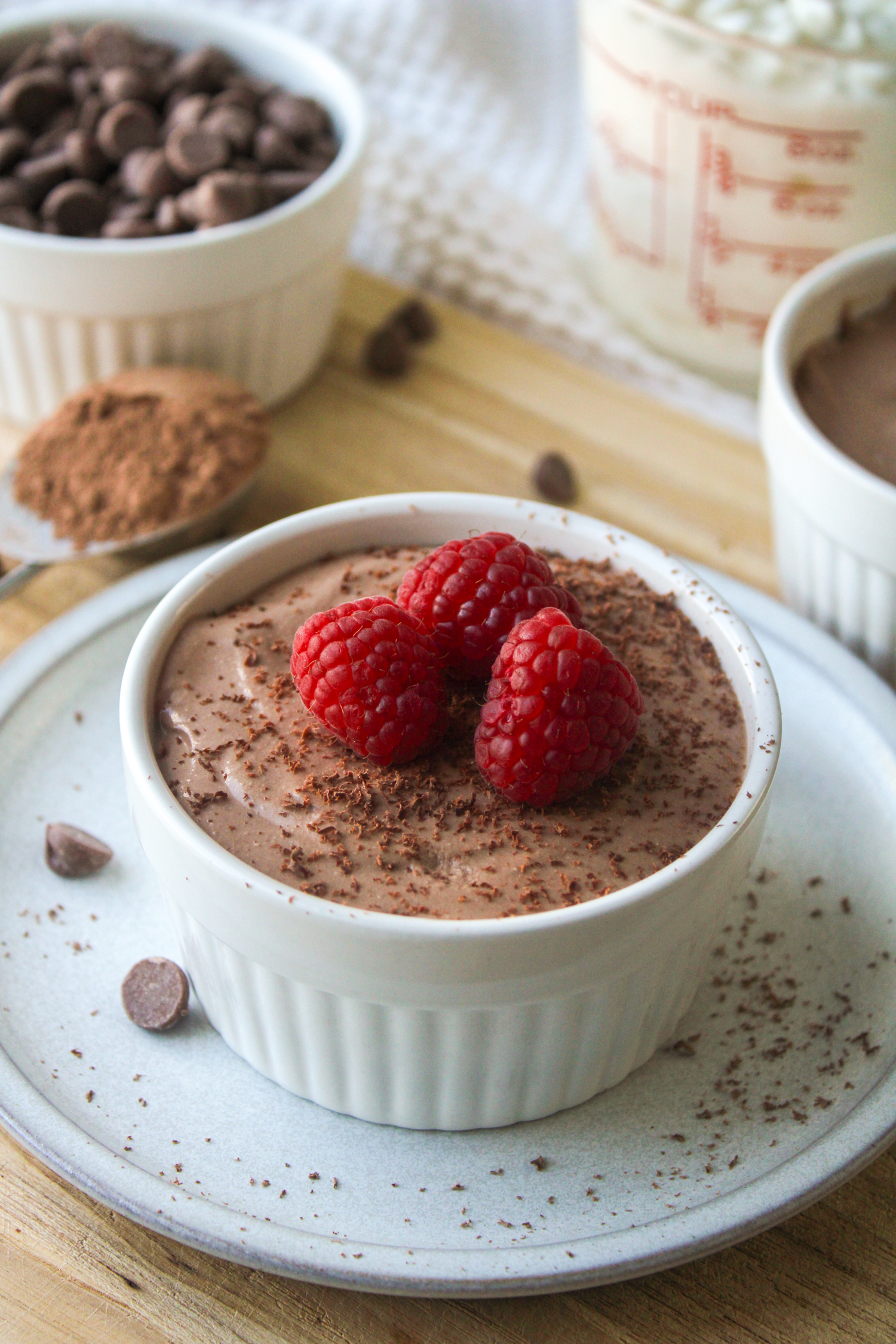 high protein chocolate mousse in a white ceramic dish, topped with chocolate shavings and raspberries