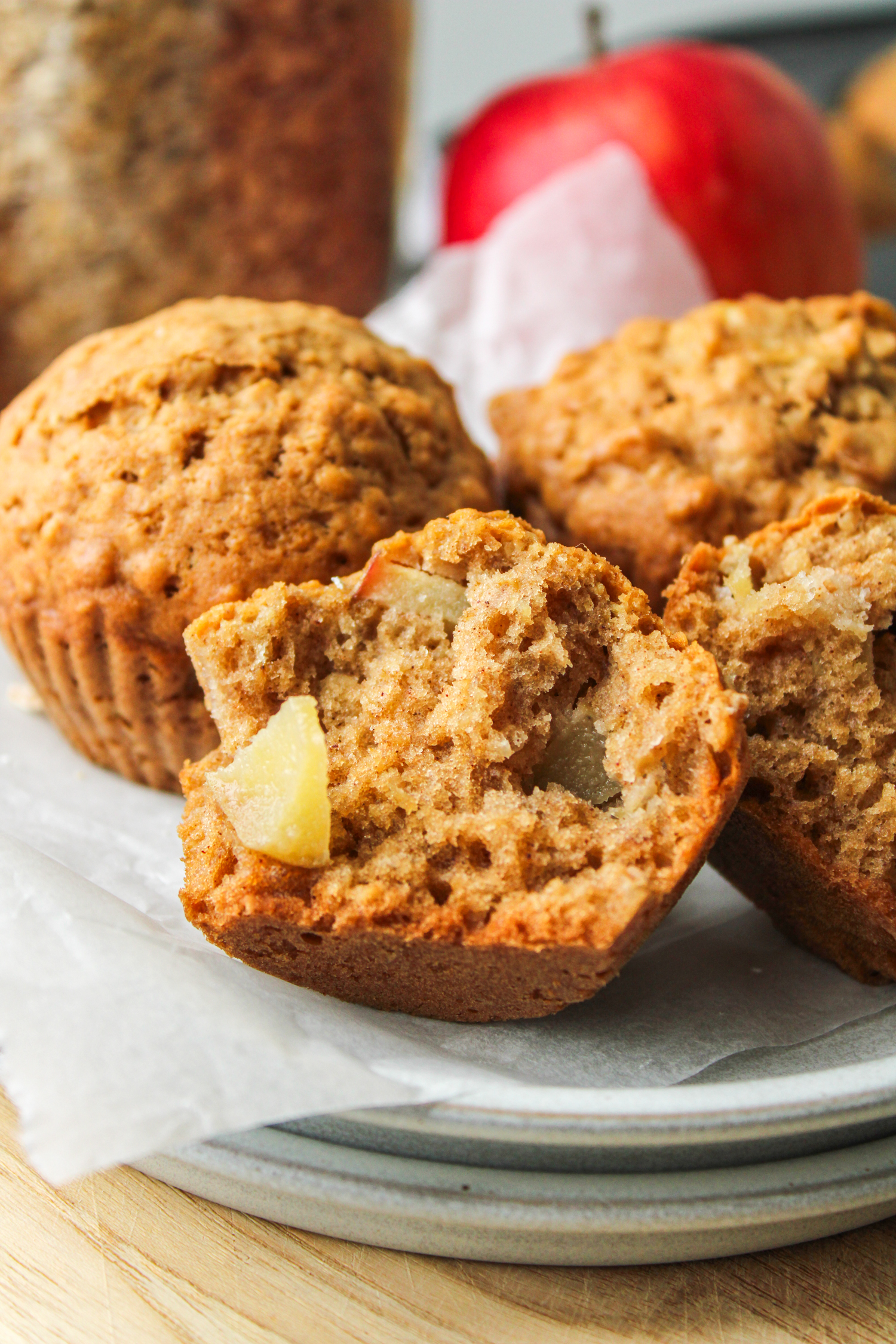 half an healthy apple oatmeal muffins on stacked white ceramic plates with other muffins surrounding it