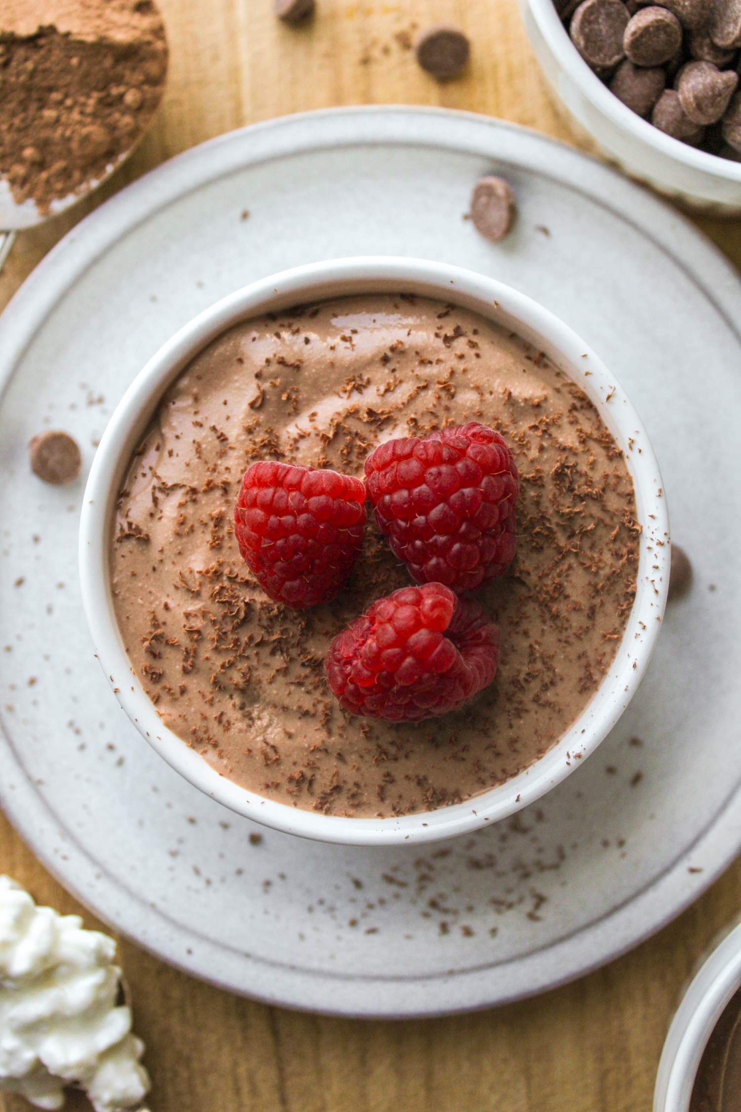 overhead shot of cottage cheese chocolate mousse in a white ceramic dish, topped with chocolate shavings and raspberries