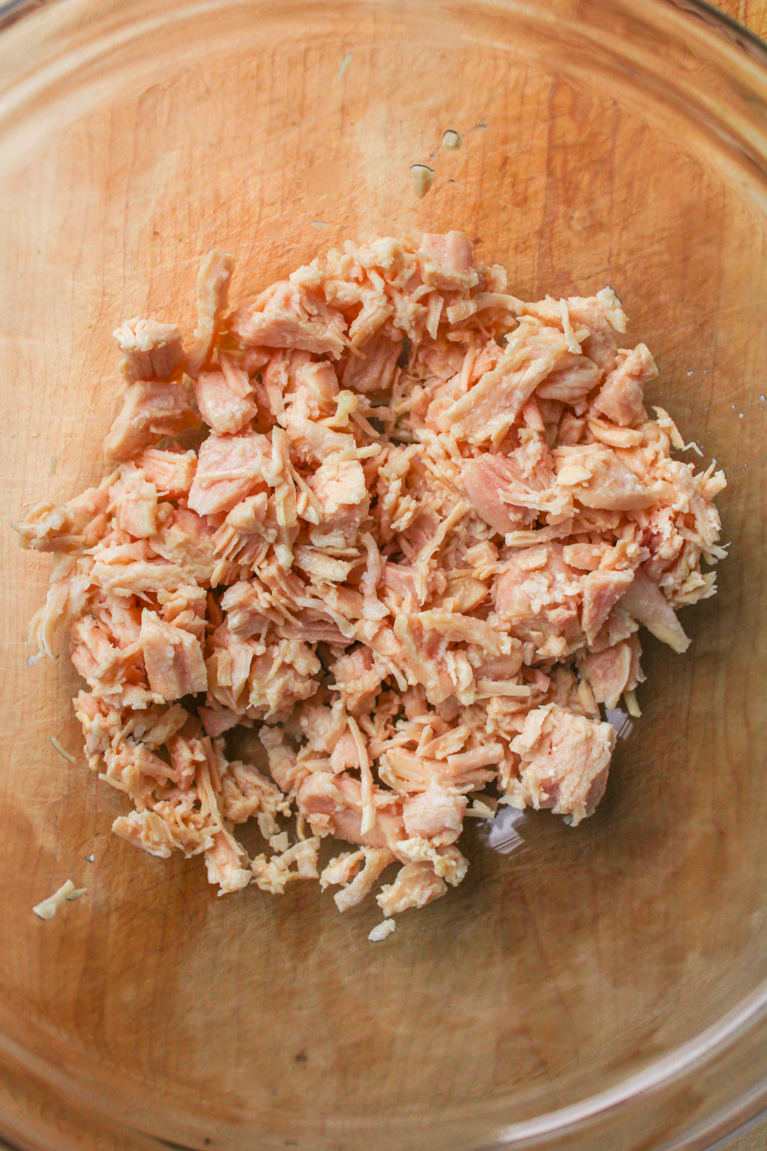 shredded chicken in a glass bowl on top of a wooden cutting board