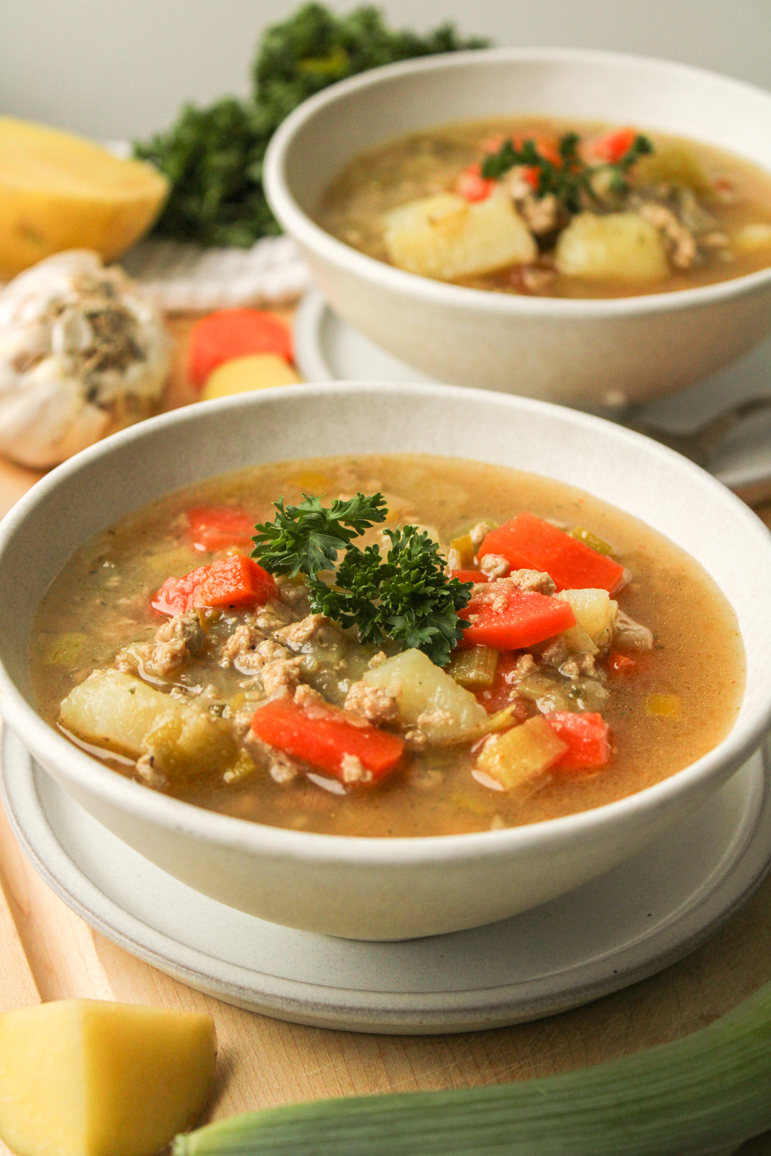 profile shot of potato leek soup with chicken topped with fresh parsley in a white ceramic bowl with another bowl of soup in the background